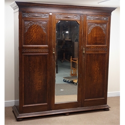  Early 20th century oak triple wardrobe, projecting cornice above three doors with carved detailing, central full length bevel edge mirror, bun feet, W200cm, H213cm, D64cm  