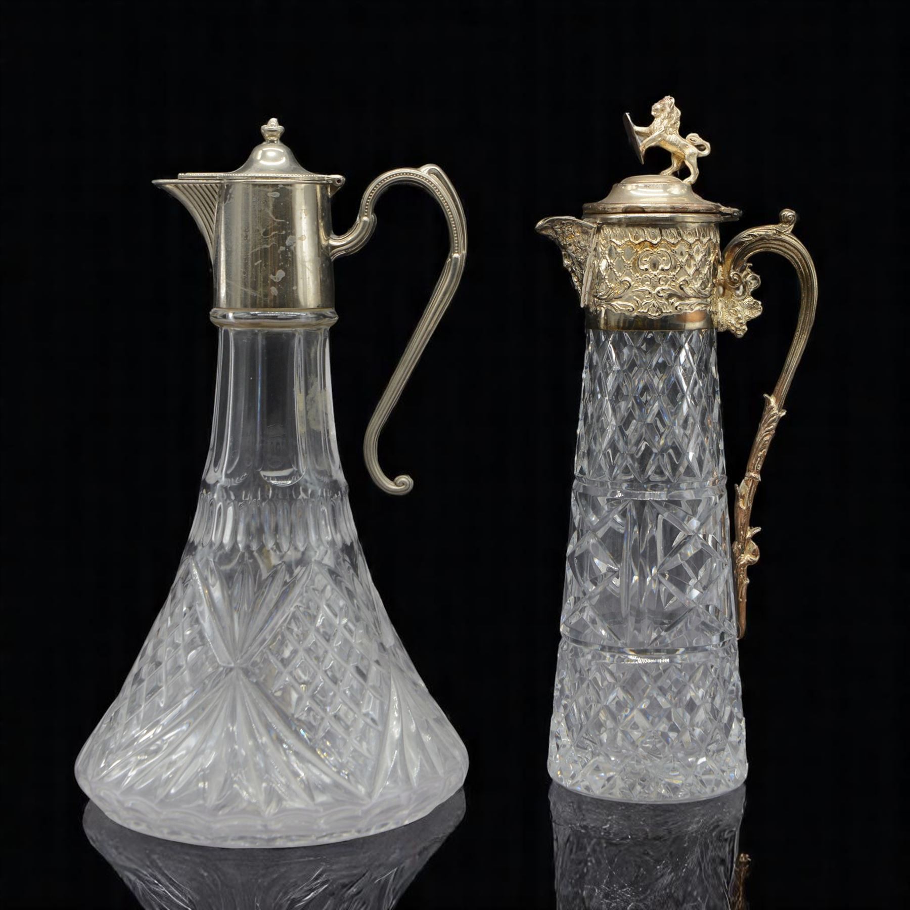 Silver plate mounted glass claret jug, the glass body of tapering form, the hinged lid a lion finial with shield shaped empty cartouche, the collar and spout cast with Bacchus face masks surrounded by grapes and vines, together with another silver plate mounted example, tallest H33cm