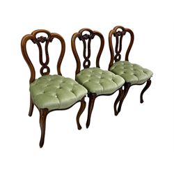 Set of six carved Victorian walnut balloon back dining chairs, button upholstered in green velvet fabric, back with foliate carved decoration supported on scroll form legs 