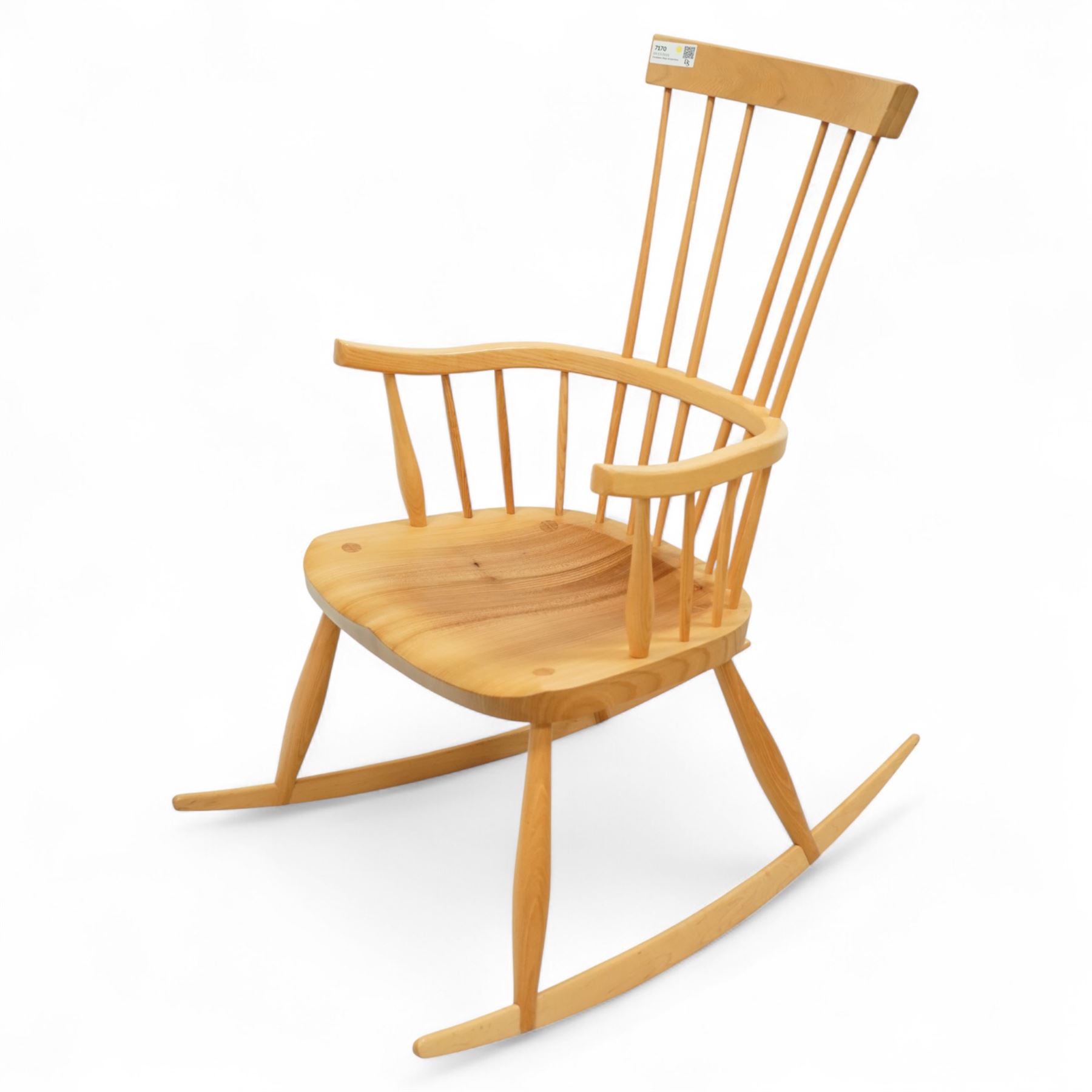Mid 20th century Windsor ash rocking armchair, in the manner of Ercol, with curved cresting rail above nine stick spindles, shaped and chamfered paddle arms, figured shaped seat, raised on turned legs joined by twin side stretchers and mounted on curved rockers