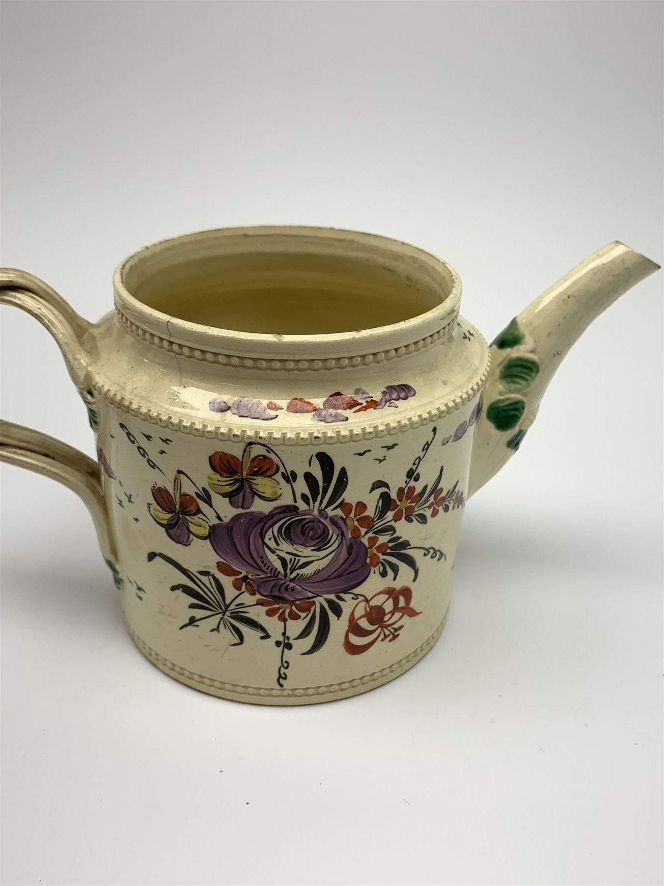 18th century creamware teapot, probably Leeds, with reeded entwined handle and floral finial to the cover, the body with hand painted polychrome decoration of figure to one side, and floral spray to the other, collectors paper label beneath inscribed Leeds Pottery, H11.5cm