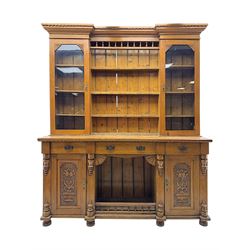 Late 19th century pine dresser, the projecting cornice with dentil and spindle moulded frieze above a three-tier plate shelves, flanked by glazed doors, the base fitted with three frieze drawers over arched apron and carved floral panelled cupboard doors, raised on turned feet