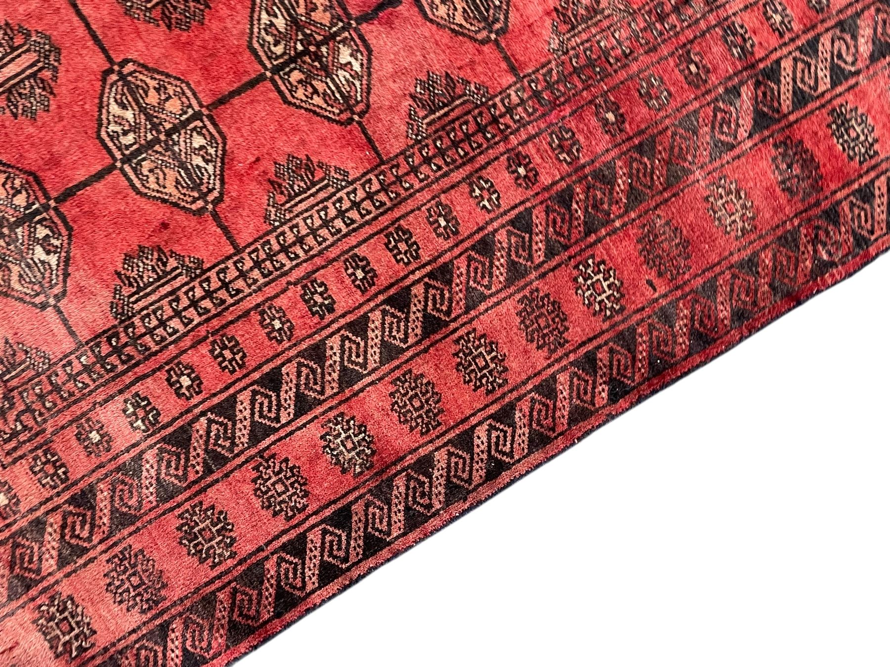 Afghan Bokhara red ground rug, the field decorated with three rows of Gul motifs, within multiple band borders decorated with trailing hook and geometric motifs 