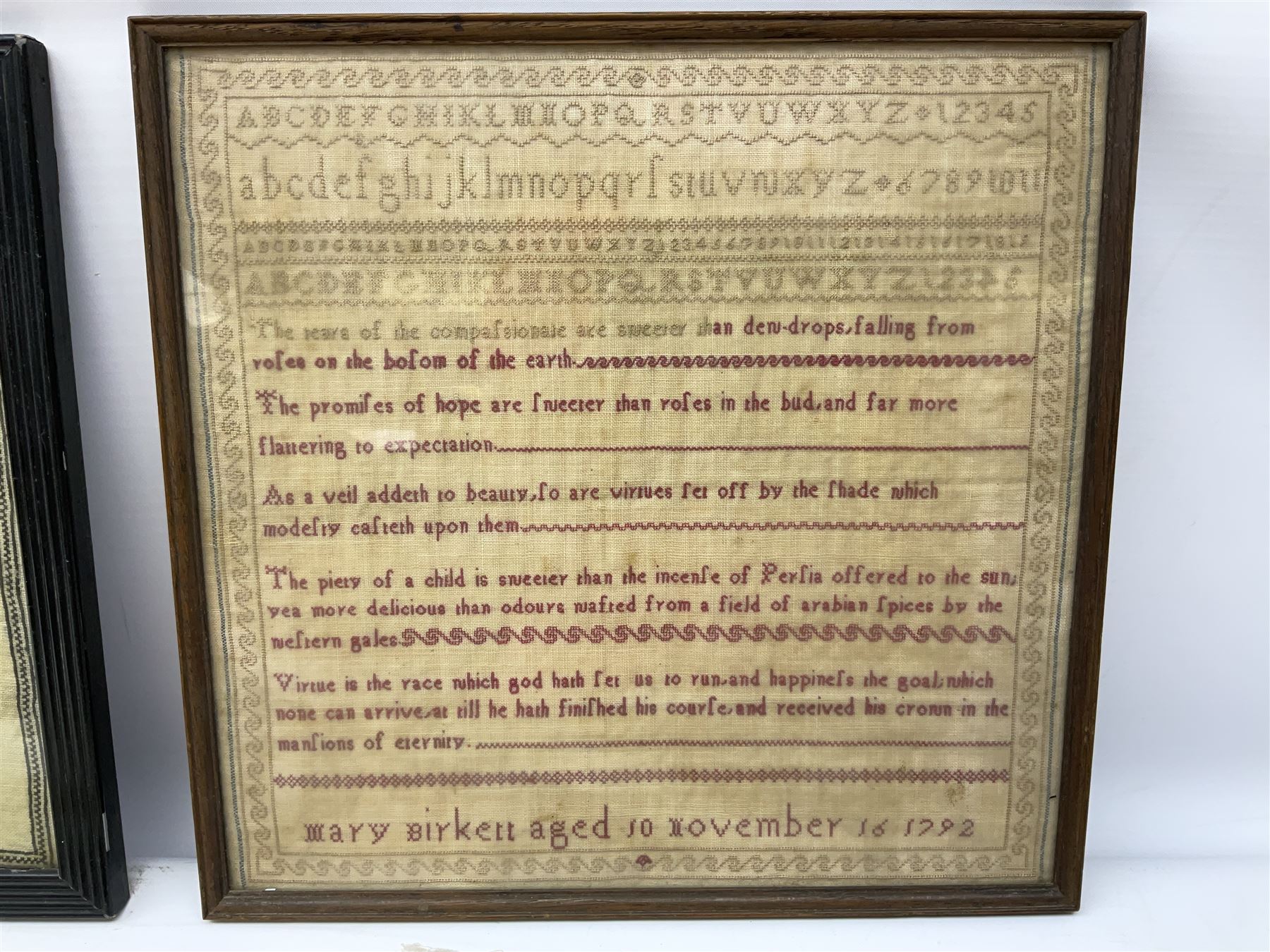 Late 18th century sampler worked with the alphabet above verses in red, by Mary Birkett aged 10 November 16th 1792, H33.5cm W34.5cm, together with another sampler worked with the alphabet above Proverbs 14:23, by Mary Anne Hainworth, Chesham, date unknown (--83), both in glazed frames, together with a quantity of Victorian and later dolls clothes to include lace examples