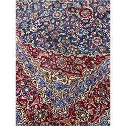 Large Persian Kashan carpet, red and blue ground, the field with central medallion surrounded by interlacing foliate and plant motifs, the border with scrolling design and decorated with flower heads