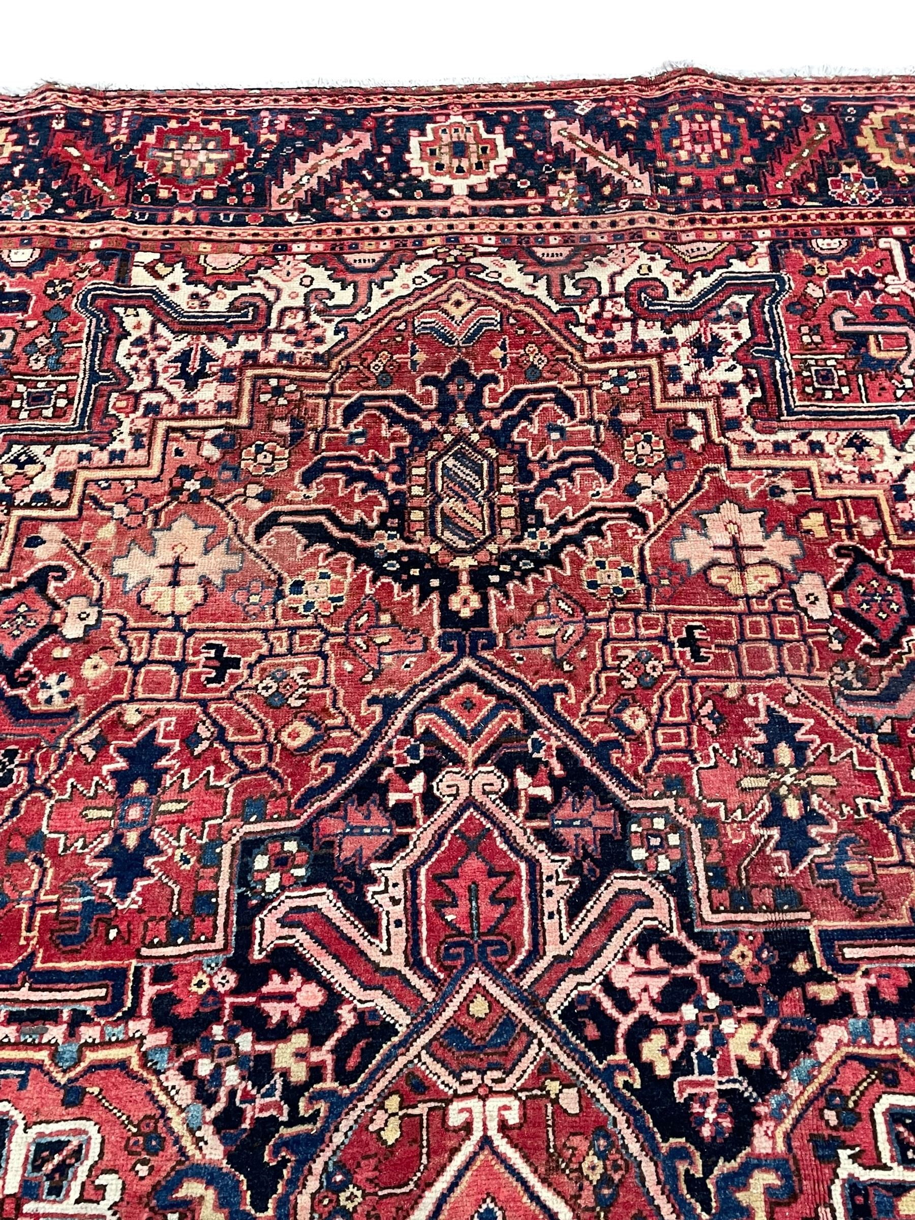 Persian Heriz crimson ground carpet, large central medallion comprising projecting palmettes with surrounding stylised plant motifs and trailing branches, the main border decorated with stylised leaf and flower head motifs within geometric pattern guard stripes
