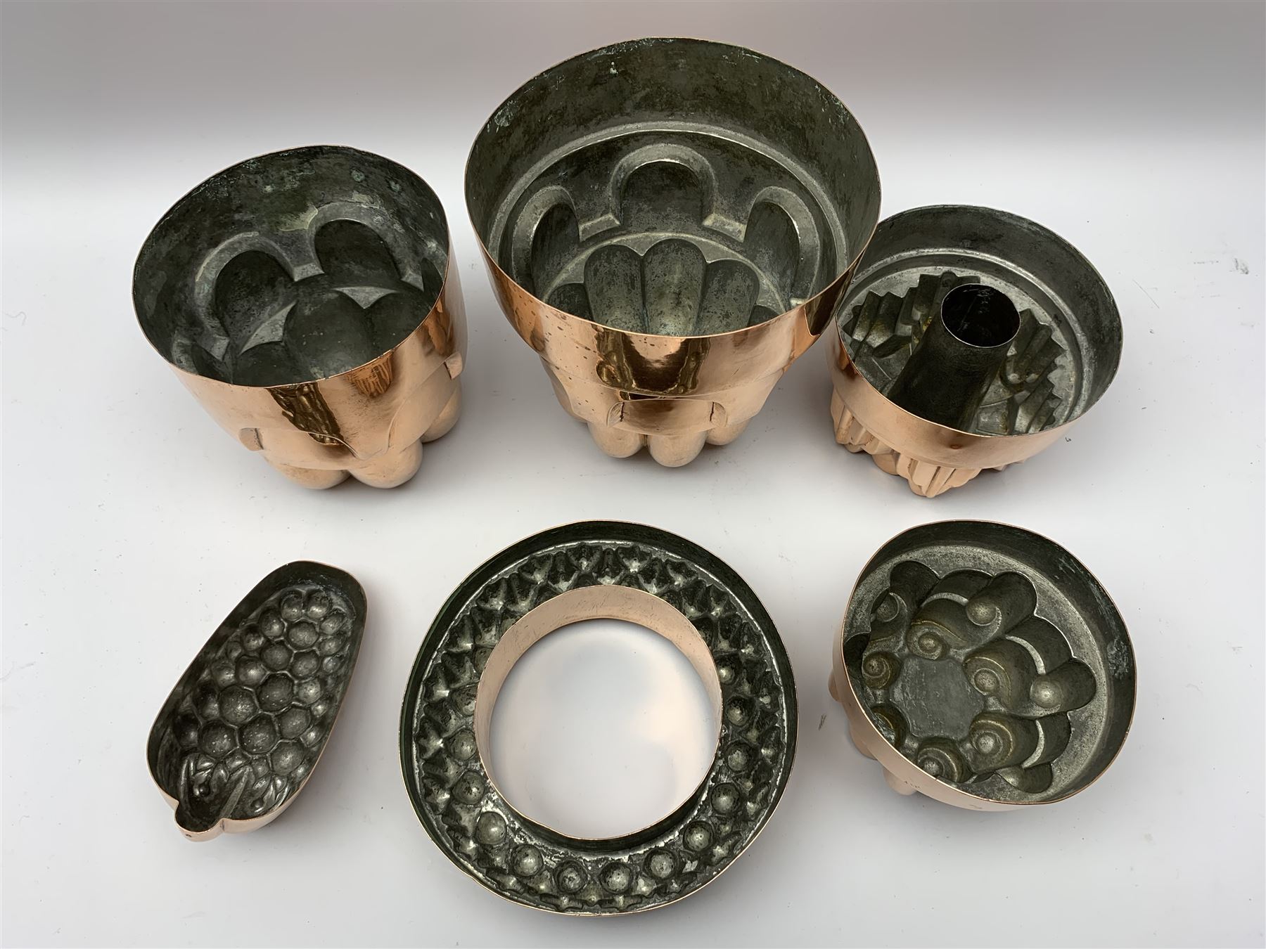 Six Victorian copper jelly moulds, five examples of castle type form, one example modelled as a bunch of grapes, largest H21cm