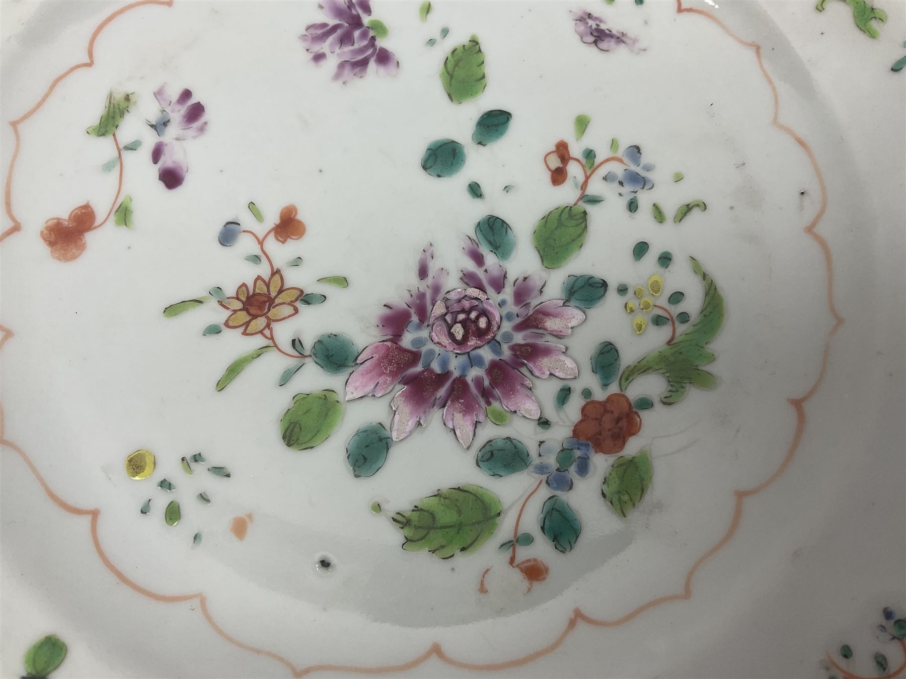 Three 18th century Chinese Famille Rose plates, the first example enamelled with blossoming peonies, rockwork and fence, the other two examples of similar design, decorated with blossoming peonies and sprigs within shaped inner borders, each approximately D23cm