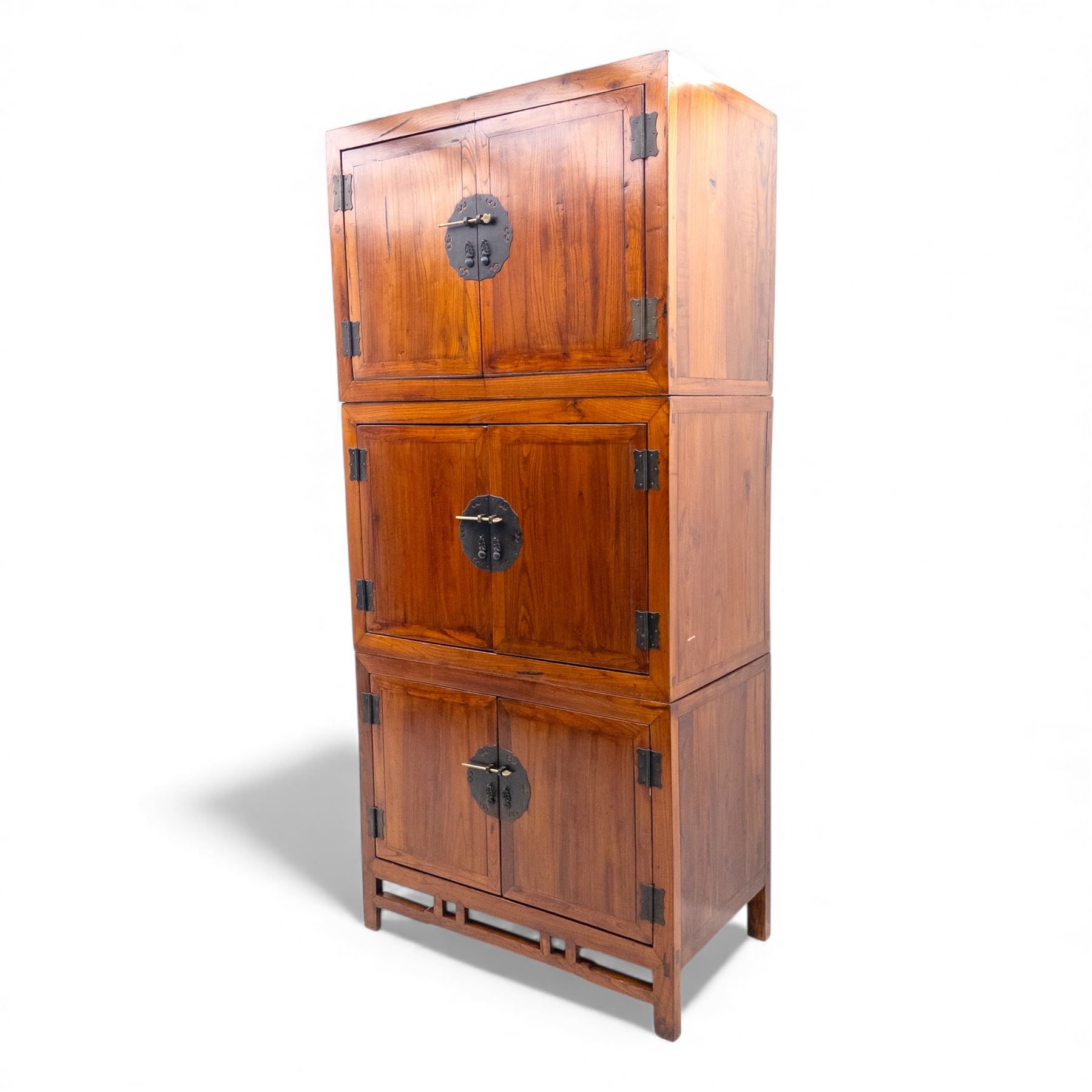 20th century Thai elm compound cabinet, formed of three stacking chests each enclosed by double panelled doors with decorative wrought metal lock plates and hinges, raised on pierced apron on stile feet