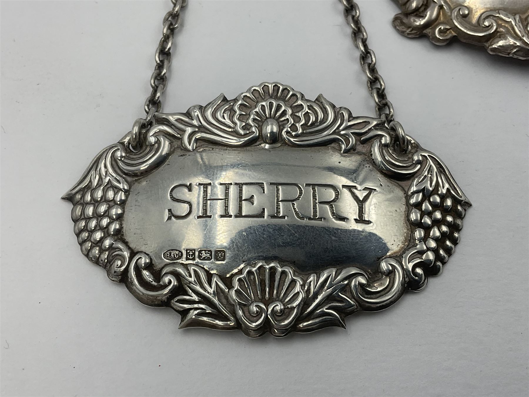 Five modern silver decanter labels, to include two sherry examples, embossed with scrolls and fruits, hallmarked W I Broadway & Co, Birmingham 1991 & 1997, a similar claret example, hallmarked S J Rose & Son, Birmingham 1973, and two plain shaped port and burgundy examples, hallmarked C Robathan & Son, Birmingham 1997 and A Haviland-Nye, London 1968