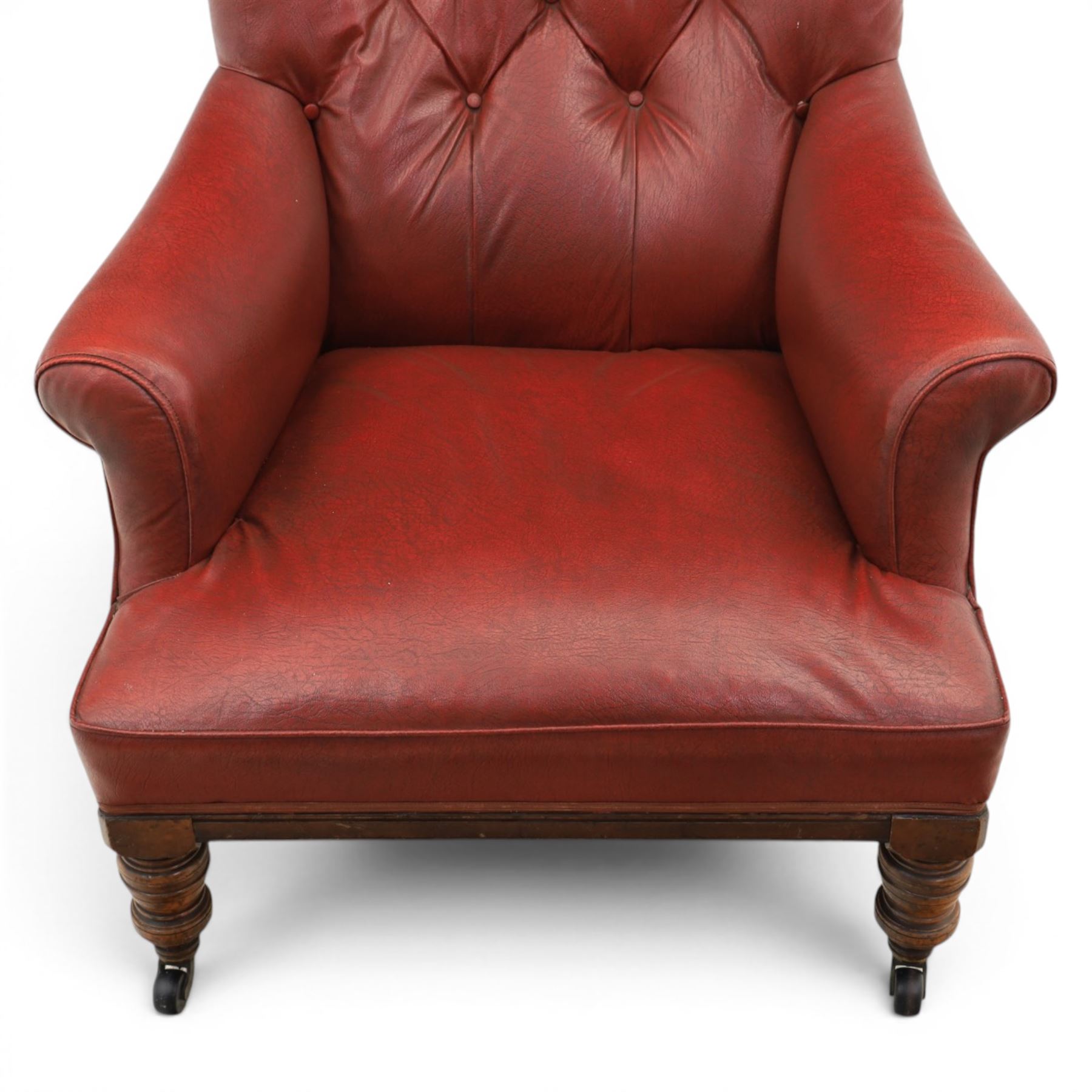 Early 20th century style oxblood red leather Chesterfield armchair, deep buttoned shaped back over padded scroll arms and loose seat cushion, raised on turned mahogany front supports with brass caps and castors