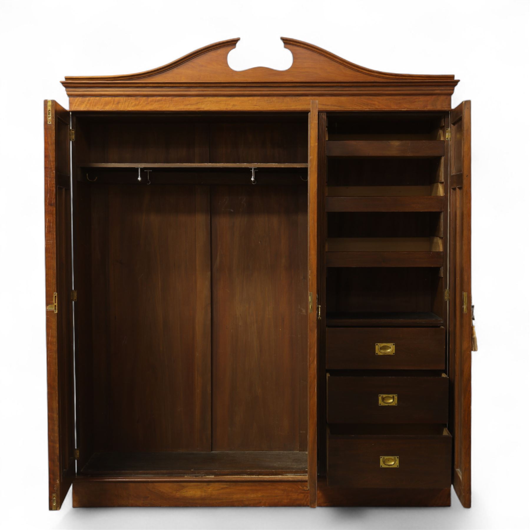 Edwardian walnut triple wardrobe, shaped broken-arch pediment over three doors comprising central mirrored door flanked by moulded raised and fielded panelled doors, interior fitted with hanging space and a bank of three open drawers above three brass recessed-pull drawers, on moulded plinth base