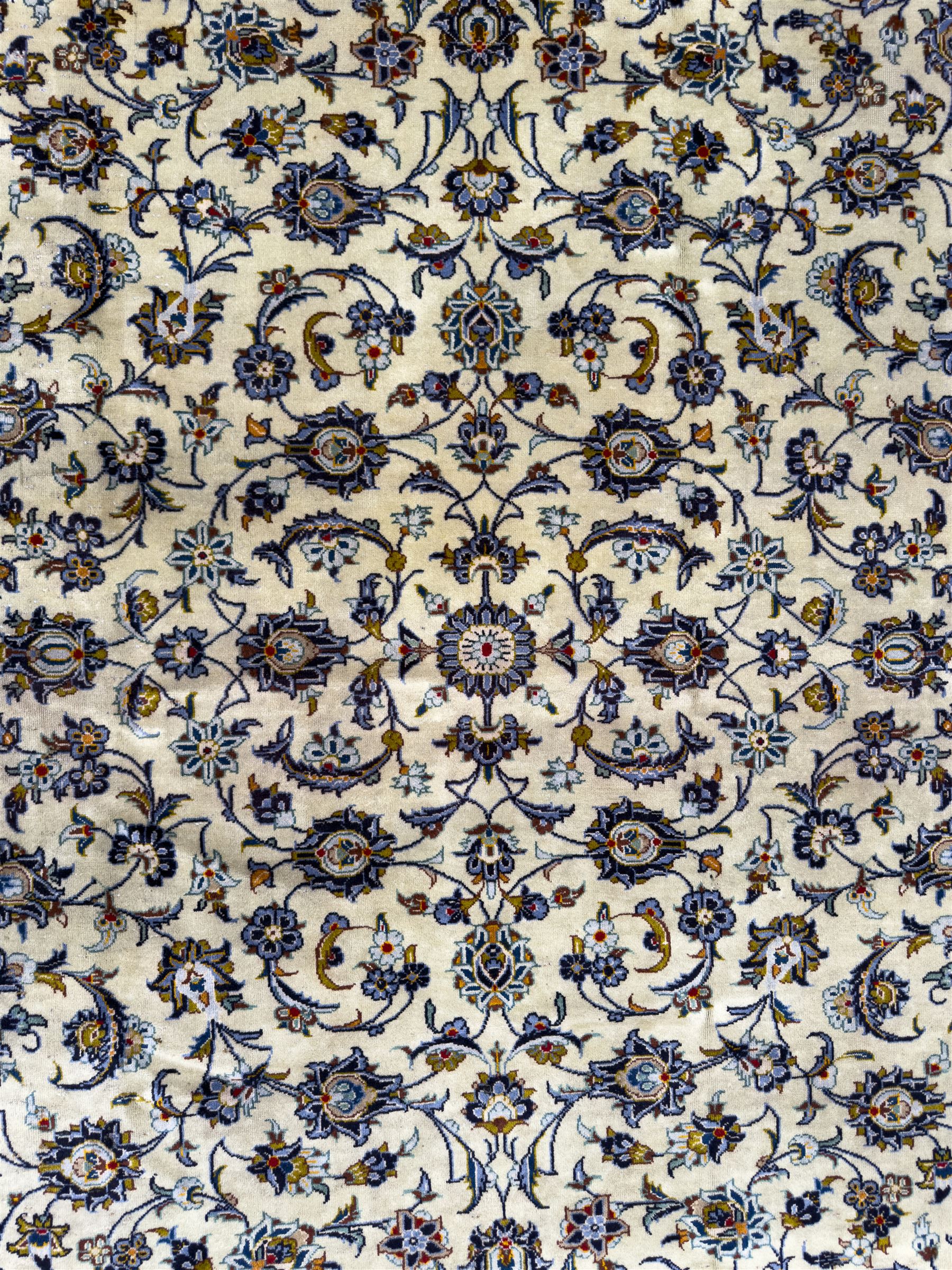 Central Persian Kashan hand-knotted carpet, ivory field with an all-over design of scrolling vines, lotus palmettes, and rosettes in shades of blue, gold, and brown within a blue ground border of palmettes and arabesques between multiple guard stripes