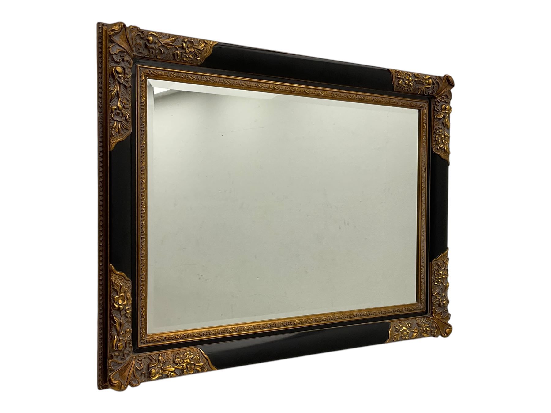 Early 20th century wall-hanging mirror, rectangular bevelled mirror plate within ebonised frame, gilt mounts to the corners carved with floral motifs 