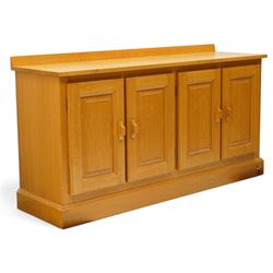Unicornman - craftsman made oak low-cupboard or sideboard, rectangular top with raised back, fitted with four panelled cupboard doors, on skirted base applied with carved unicorn signature, by Geoff Gell of Coxwold