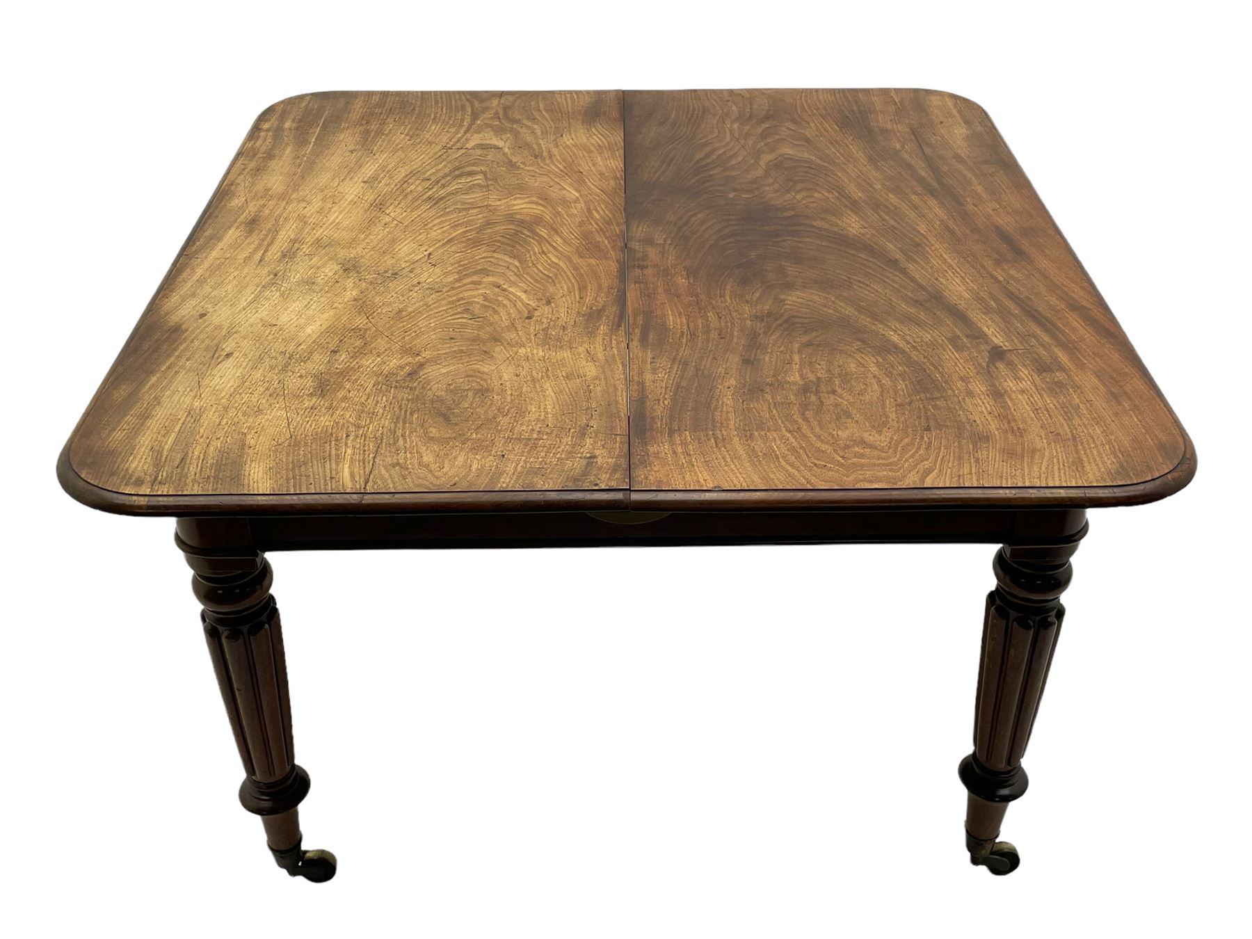 Early 19th century figured mahogany extending dining table, the rectangular top with moulded edge and rounded corners, pull-out action with three additional leaves, raised on turned and lobe carved supports with brass cup castors