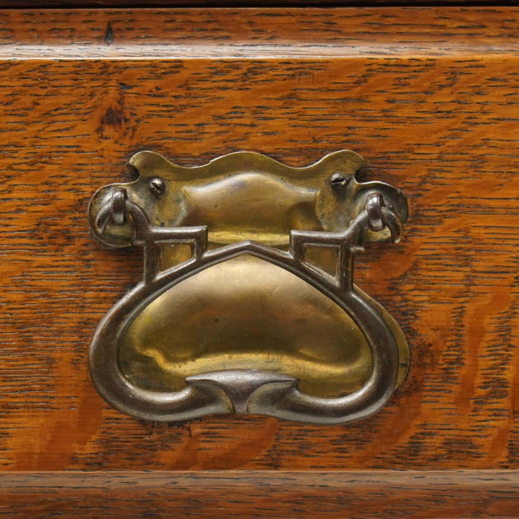 Arts and Crafts oak dresser, projecting moulded cornice above three glazed panels with coloured leaded glass floral panels, flanked by two glazed doors enclosing two adjustable shelves, open mirrored recess below with mirrored back, the base fitted with two short drawers over two central drawers flanked by carved panelled cupboard doors, ornate brass handles, raised on tapering square legs
