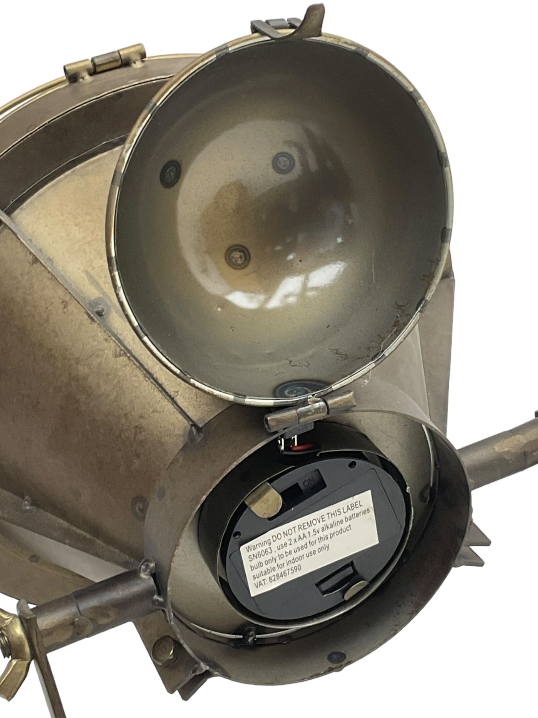 Industrial tripod spotlight, with a metal shade and wire guard, supported by a height-adjustable tripod base, the head equipped with an adjustable tilt mechanism