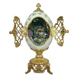 Franklin Mint The Emerald Isle Collector Egg, the egg decorated with embossed shamrocks upon a cream ground, with a gilded shamrock finial, accents and openwork door, opening to reveal a miniature landscape scene, upon three gilded feet set with green paste stones, with certificate of authenticity H23cm, 