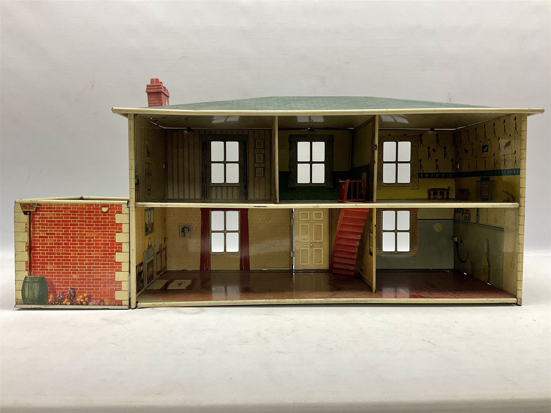 Mid-20th century Mettoy tin-plate double-fronted two-storey doll's house, the front elevation with five unglazed windows flanked by green shutters, central opening door, open back giving access to five rooms together with an attached garage, 60cm wide