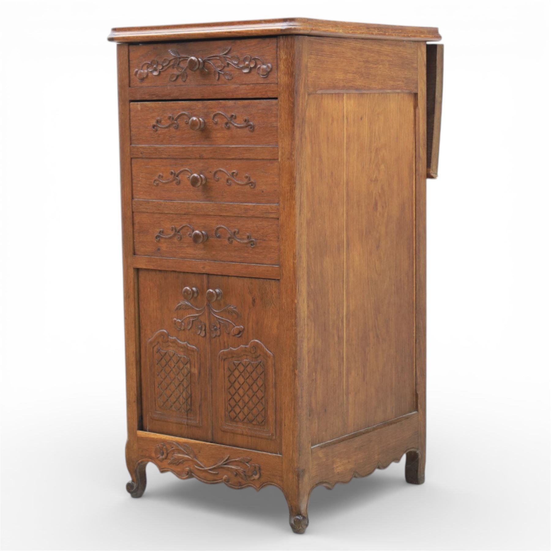 20th century French style oak bedside chest of pedestal form, the top with rounded moulded edge with drop leaf to the back, above five carved drawers with applied scroll ornament and turned knobs, the cupboard base with twin carved doors with diamond lattice panels, with shaped apron and bracket feet