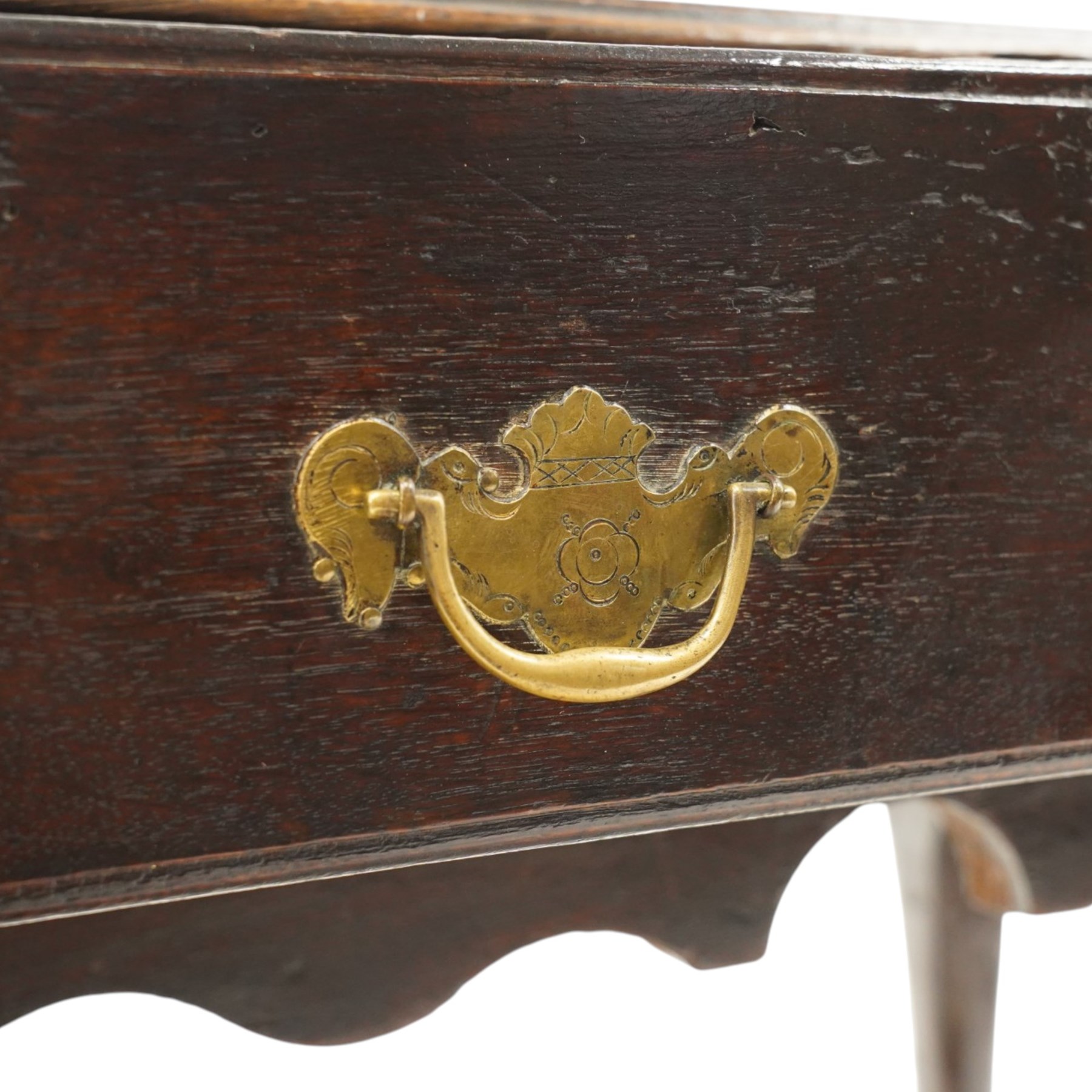18th century oak lowboy, the rectangular top with moulded edge and eared front-corners, fitted with single drawer with pressed brass handle-plates, shaped apron over cabriole supports and pad feet