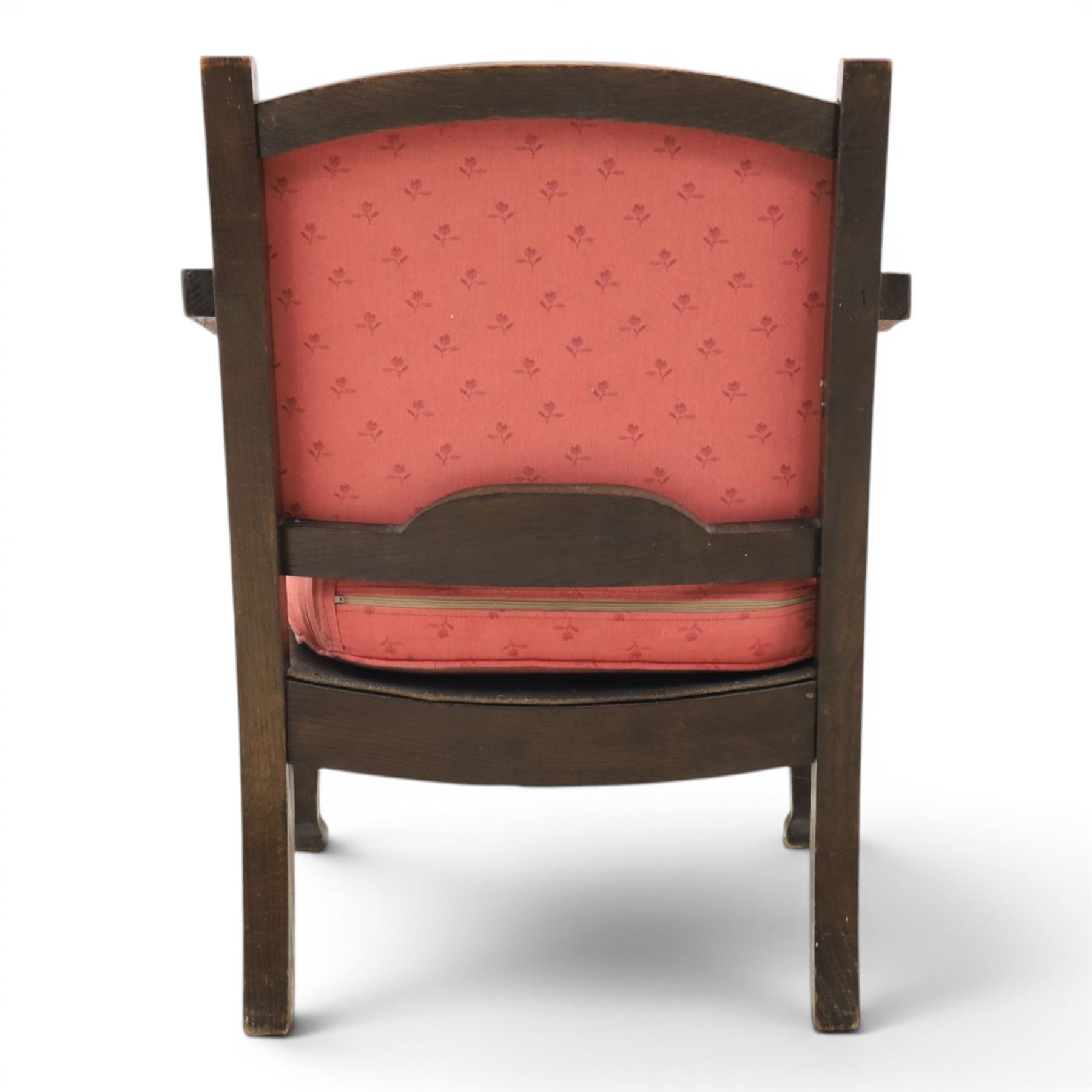 Early 20th century small oak open armchair, arched upholstered back with brass stud border over shaped seat cushion upholstered in pink foliate fabric, shaped open arms on square supports