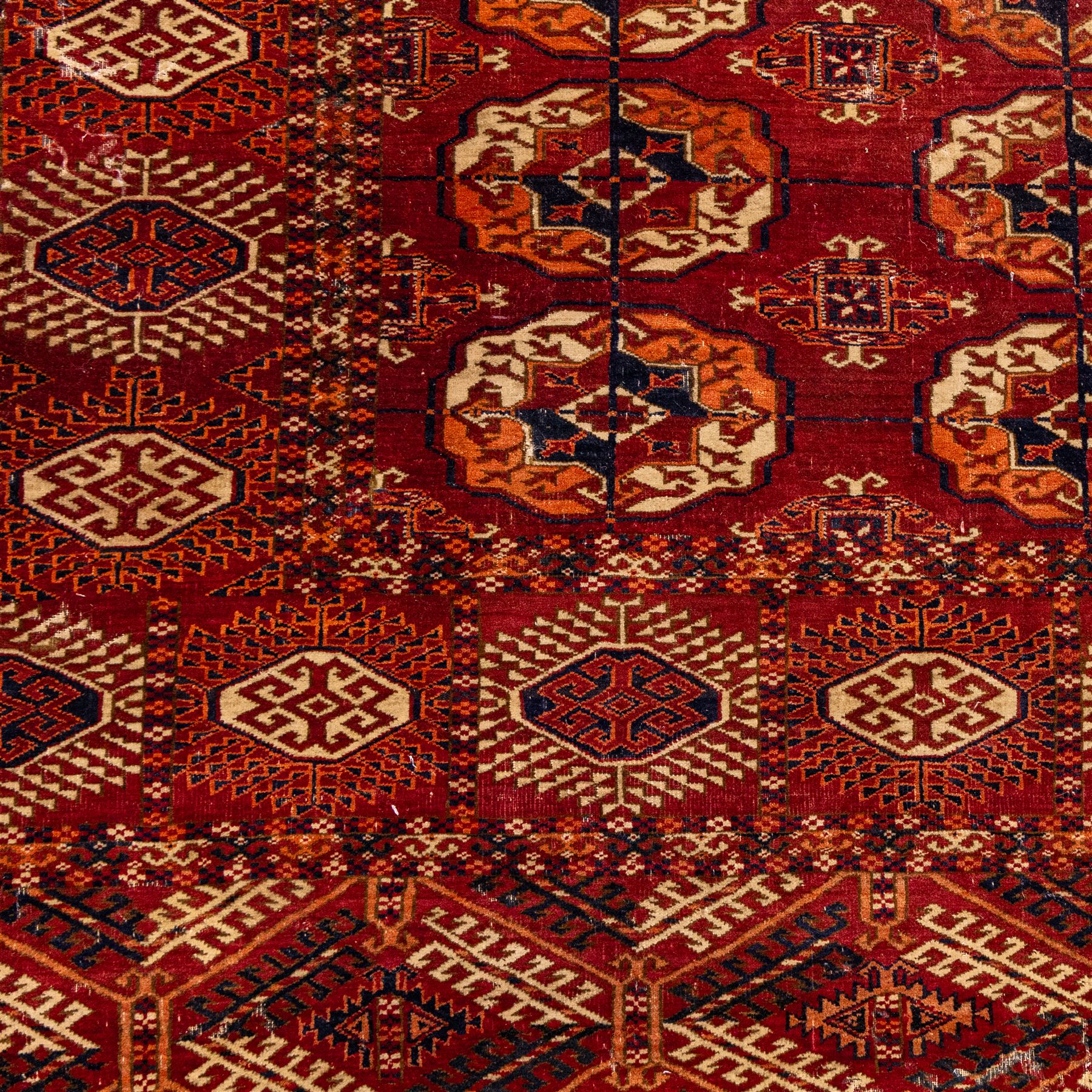 Vintage Bokhara hand-knotted rug, madder field woven in rows of octagonal Tekke guls arranged in vertical columns, each enclosing angular cruciform devices and tribal motifs, divided by narrow indigo lines, within multiple geometric borders incorporating stepped lozenges and latch hook devices, with cotton fringe ends 