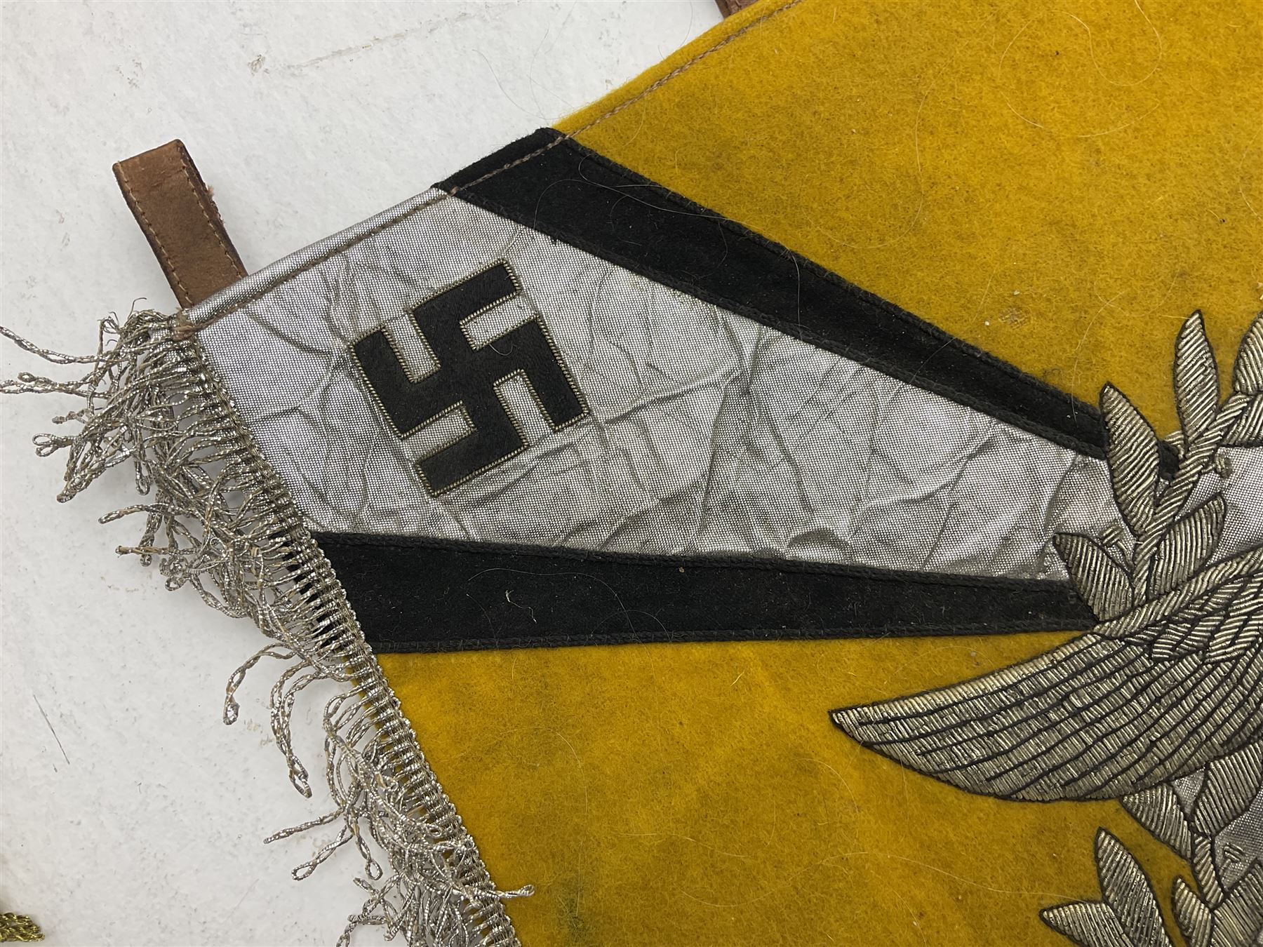 Two replica German Luftwaffe trumpet banners, one heavily silver wire embroidered with Luftwaffe eagle in a wreath, on an amber, white and black rayed background, , with silver wire tasselled border and four leather hanging loops, approx. 50 x 49cm; the other slightly larger heavily gold wire embroidered with the Luftwaffe eagle on a plain amber ground with gold wire tasselled border and two hanging loops (2)