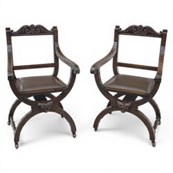 Late 20th century stained beech Savonarola chair, the carved crest rail and open arms above an upholstered leather seat, raised on an X framed base with carved foliate and mask decoration, joined by turned stretcher and ending in castors