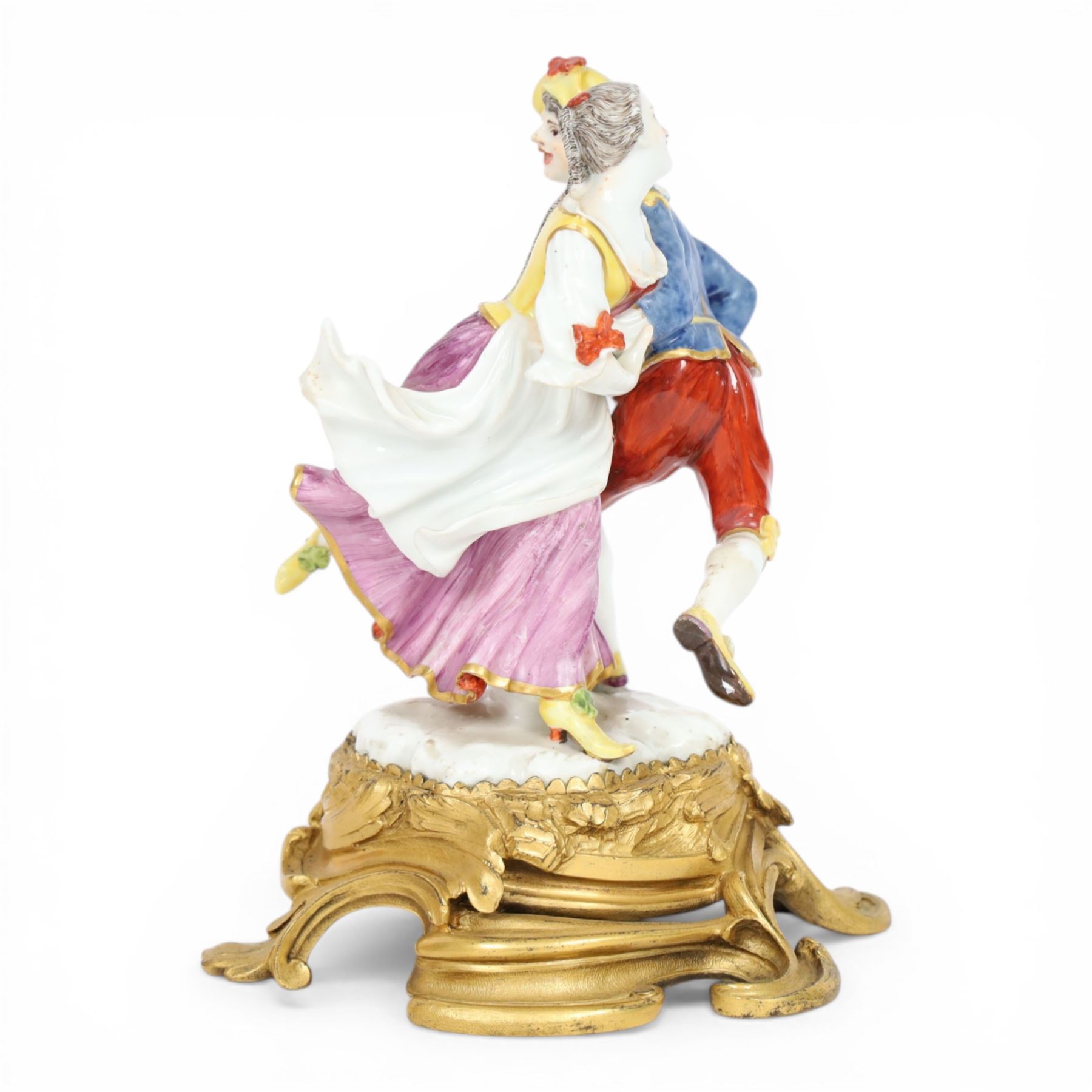Mid 18th century Meissen figure group, The Tyrolean Dancers, circa 1740, modelled as two swirling figures with their arms linked, he in yellow hat with red rosette, blue jacket, red breeches with red rosette, and yellow shoes with green rosette, she in white blouse with red ribbons, yellow and red bodice, white apron over puce skirt and yellow shoes with green rosettes, her hair fashioned into two plaits secured by red ribbon, upon a shaped mound base, within a scrolling gilt metal mount, with blue crossed swords mark to base, overall H19cm
