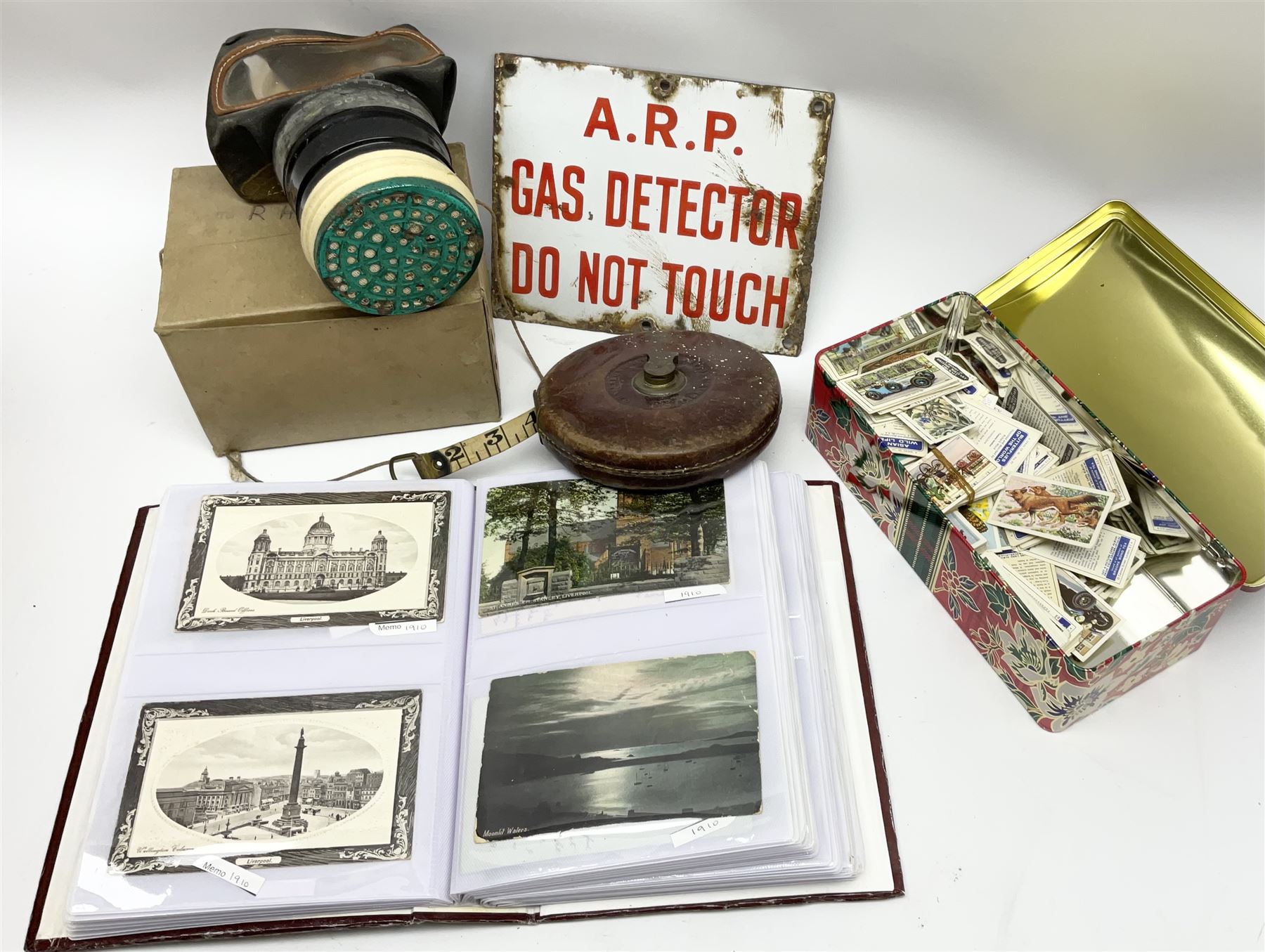 Postcards including WW1 silk postcards, local interest and photographic postcards, gas mask in box, material tape measure and metal sign. 