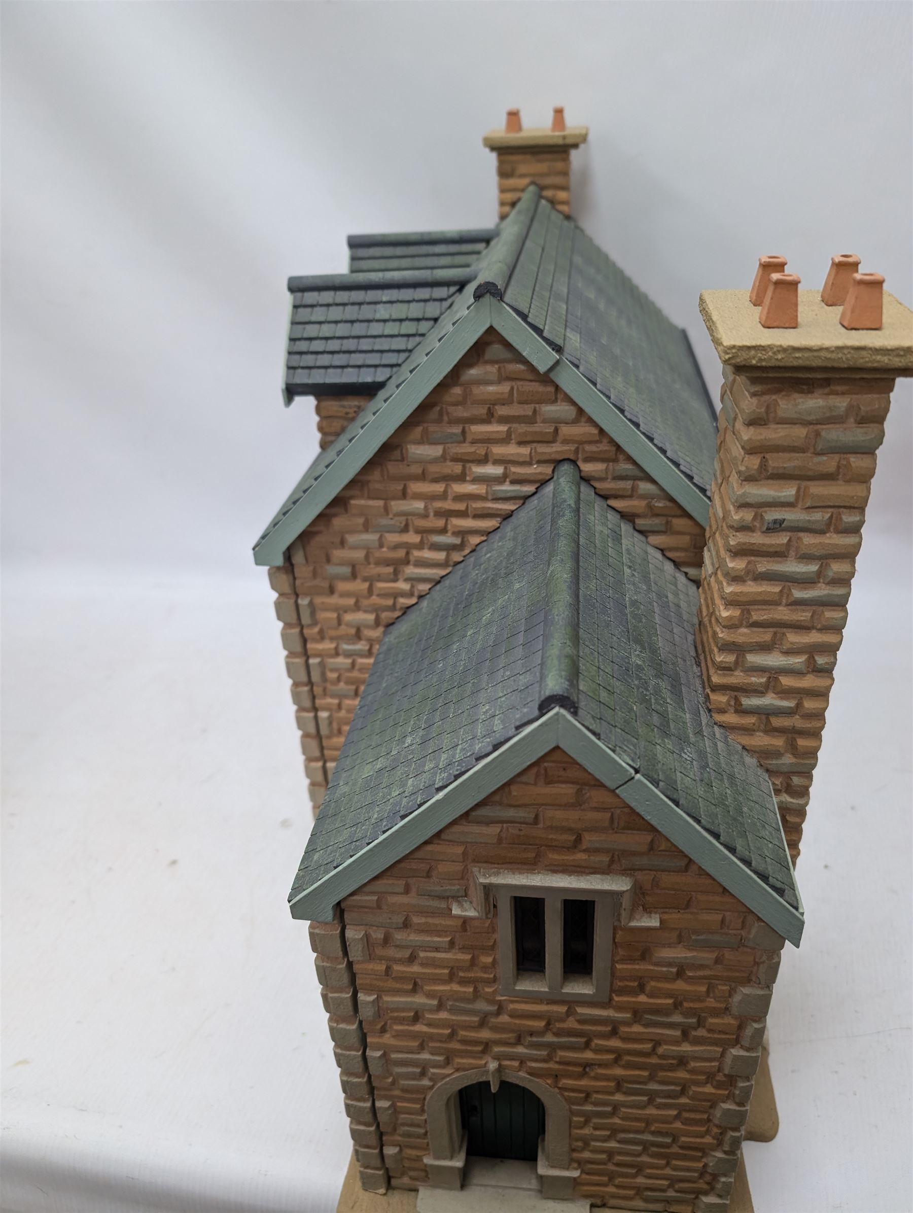 1:24 scale stone effect three-storey cottage dolls house, with green arched door and lattice effect windows, decorated to the interior with wooden floors, wired lighting and fire places, H45cm, W57cm, D26cm