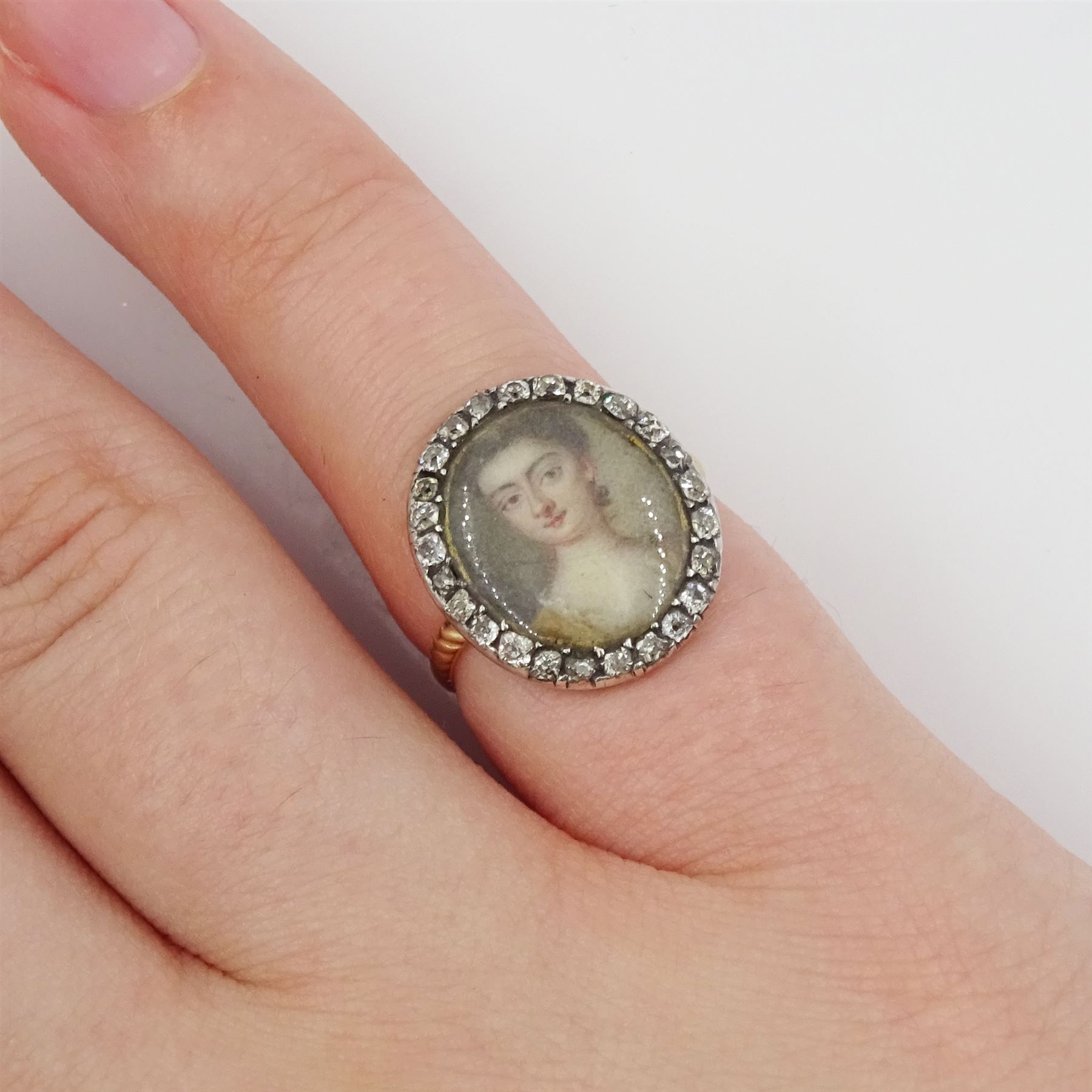 18th/ 19th century gold diamond portrait ring, set with an oval miniature of a woman on ivory, under a glazed panel, with old cut diamond surround and rope twist shank. This lot has been registered for sale under Section 10 of the APHA Ivory Act