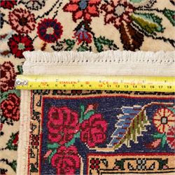 Two small rugs, an ivory ground example decorated with a central floral medallion and scattered rose sprays, enclosed by a navy foliate border (62cm x 101cm), and a crimson pictorial mat worked with seated figures, an animal and birds amongst flowering plants (45cm x 79cm) (2)