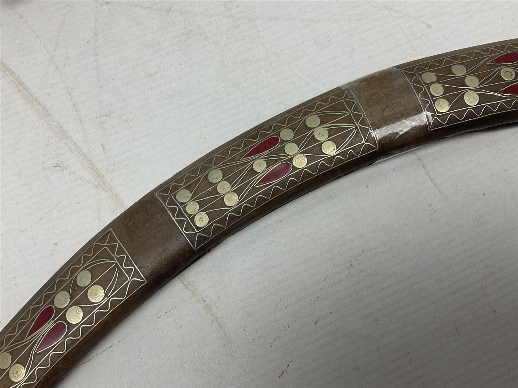 Late 19th/early 20th century Moroccan nimcha dagger-sword, the 40cm curving steel blade with engraved decoration on both sides; shaped hardwood hilt inlaid with brass, white metal wires and red coloured panels; in similarly inlaid scabbard L61cm overall