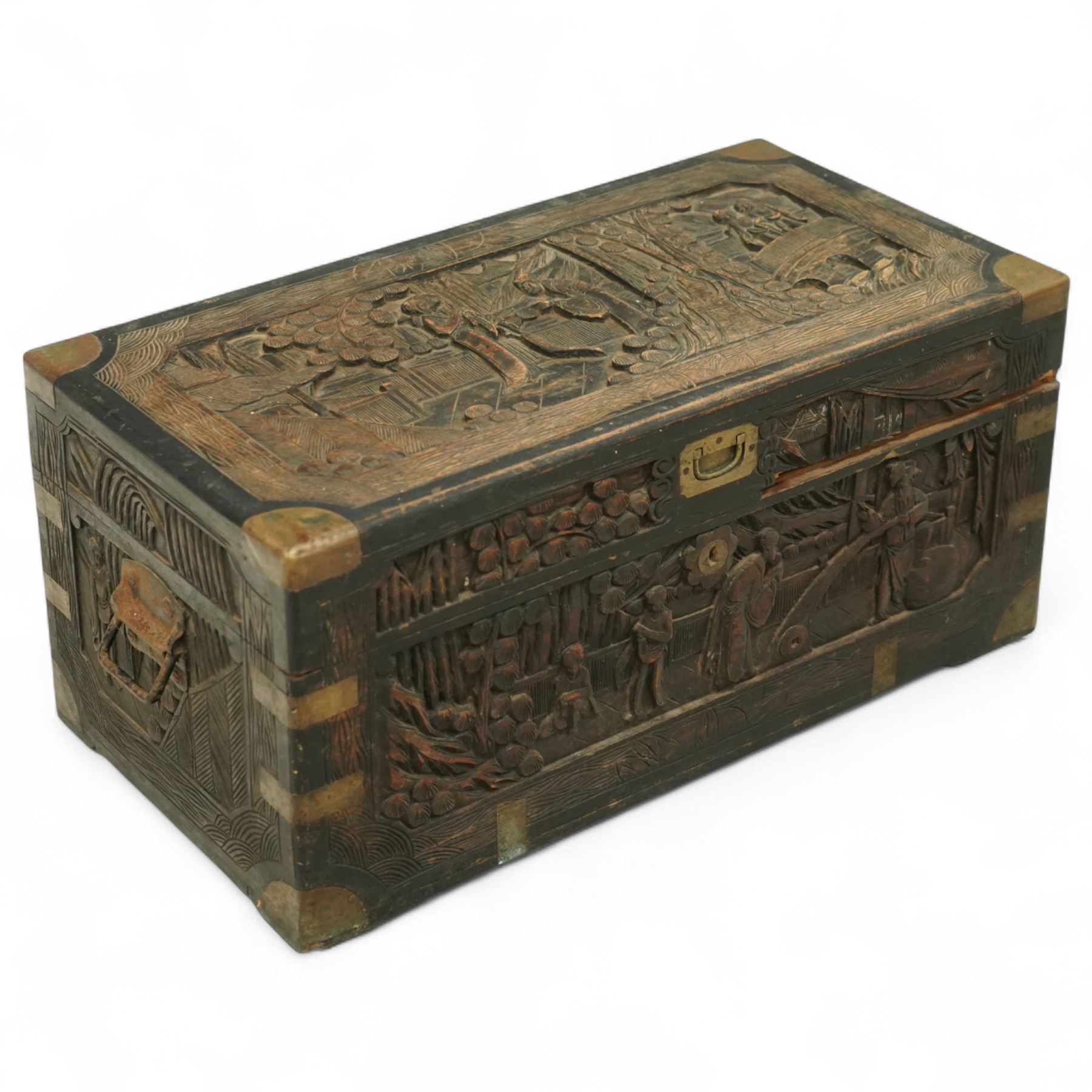Early 20th century Chinese brass bound camphor wood coffer, rectangular form, the hinged lid and sides deeply relief carved with figures in landscape scenes within geometric borders, fitted with brass corner mounts and recessed carry handles