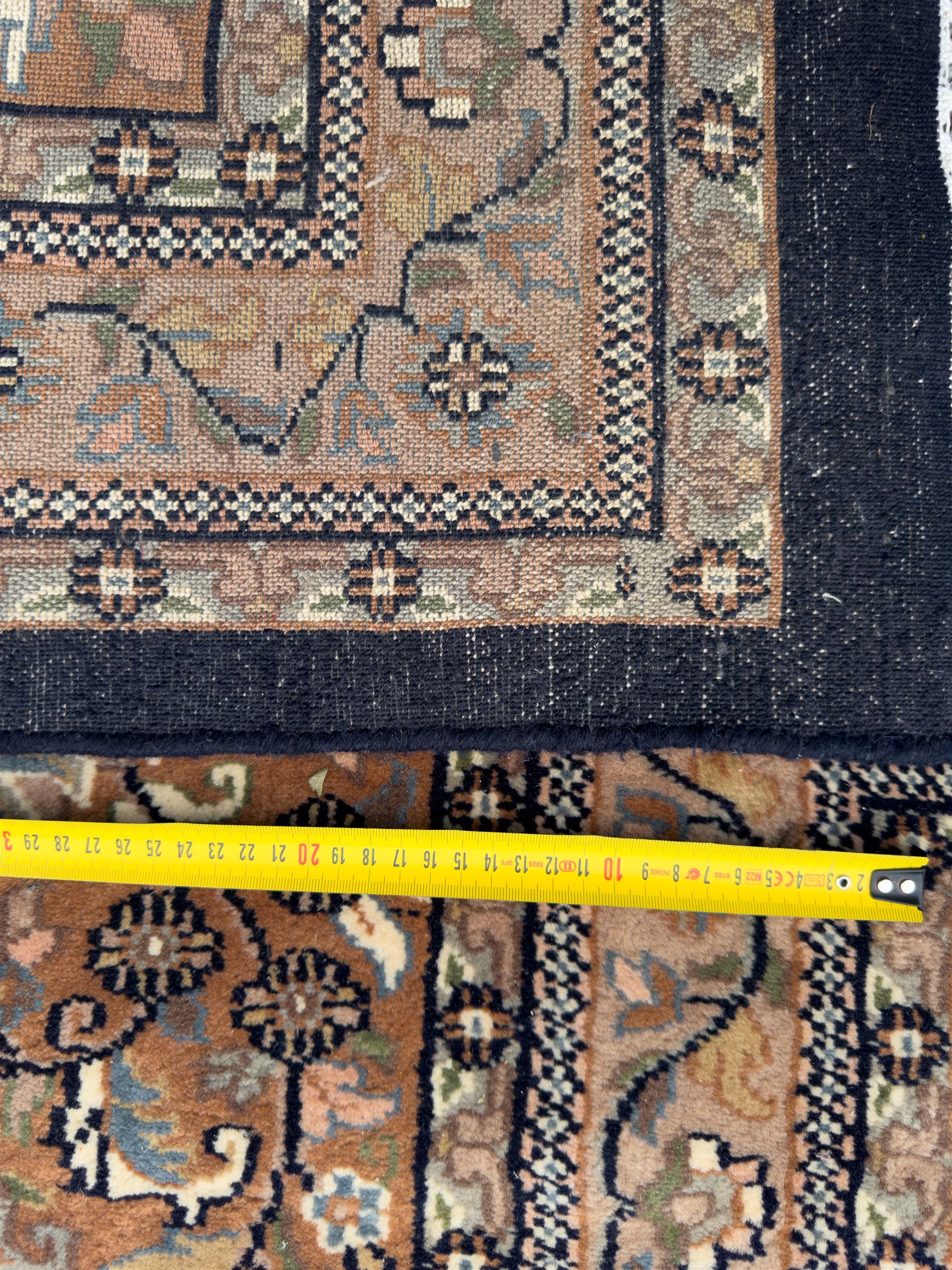 Large Persian indigo ground rug, the busy field decorated with trailing branches and flower heads, peach border decorated with palmettes -