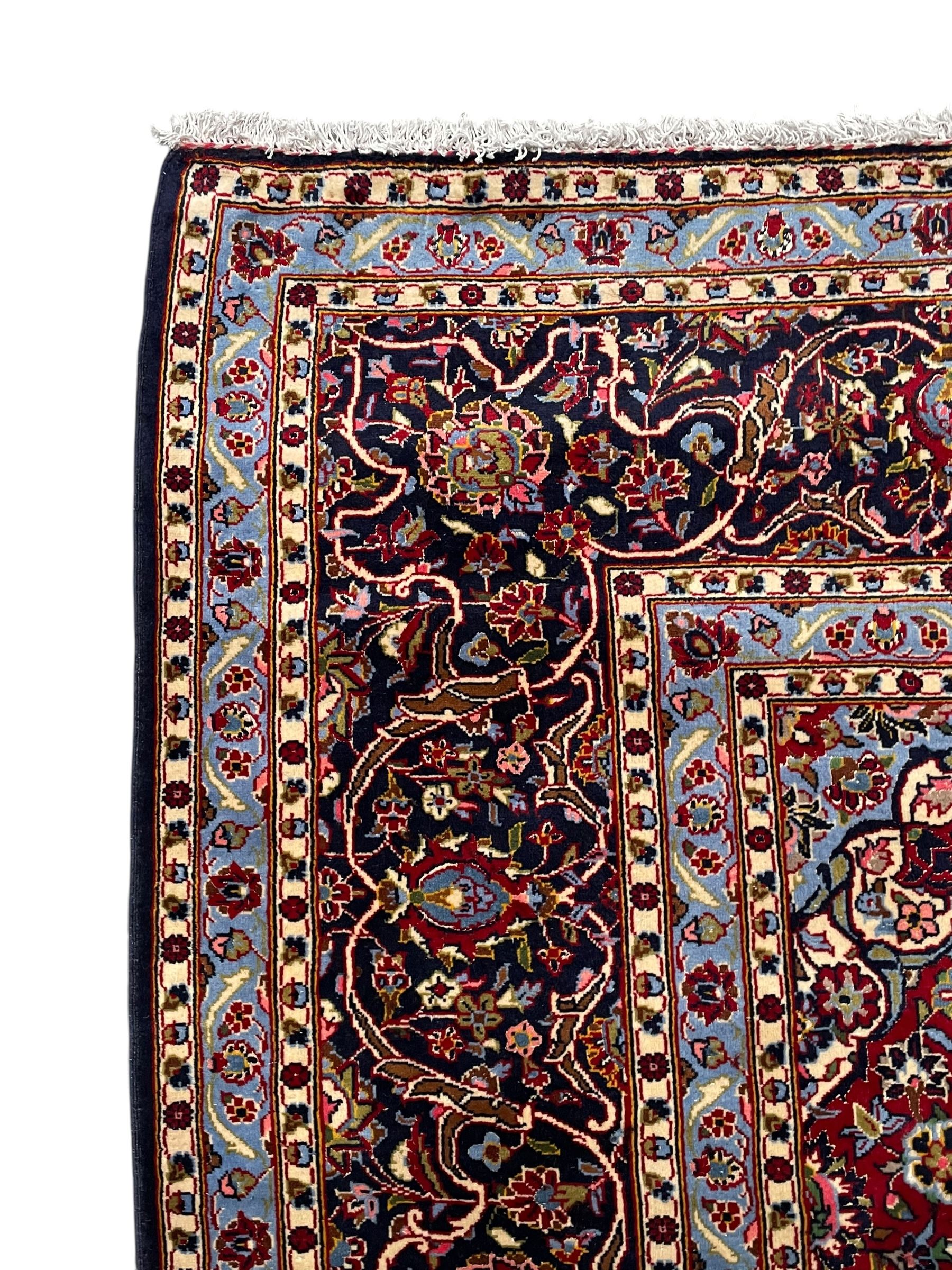 Persian Kashan indigo ground carpet, central floral pattern medallion surrounded by a densely decorated field depicting trailing branches with leaves and palmettes, scrolling border decorated with stylised plant motifs, within floral pattern guard stripes 