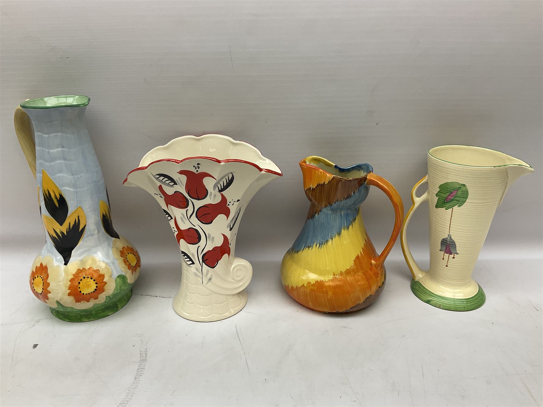 Group of Art Deco ceramics, comprising Wadeheath jug painted in spiralled bands of blue, orange, yellow and brown, shape no. 707784, Royal Doulton Caprice pattern twin handled bowl, no. D5358, Arthur Wood wall pocket of typical stylised fan form with painted floral decoration, Arthur Wood vase of cornucopia form with red and grey floral decoration, Wadeheath jug of ribbed form with stylised handle, and two Hancock's Ivory Ware jugs, tallest example H26cm