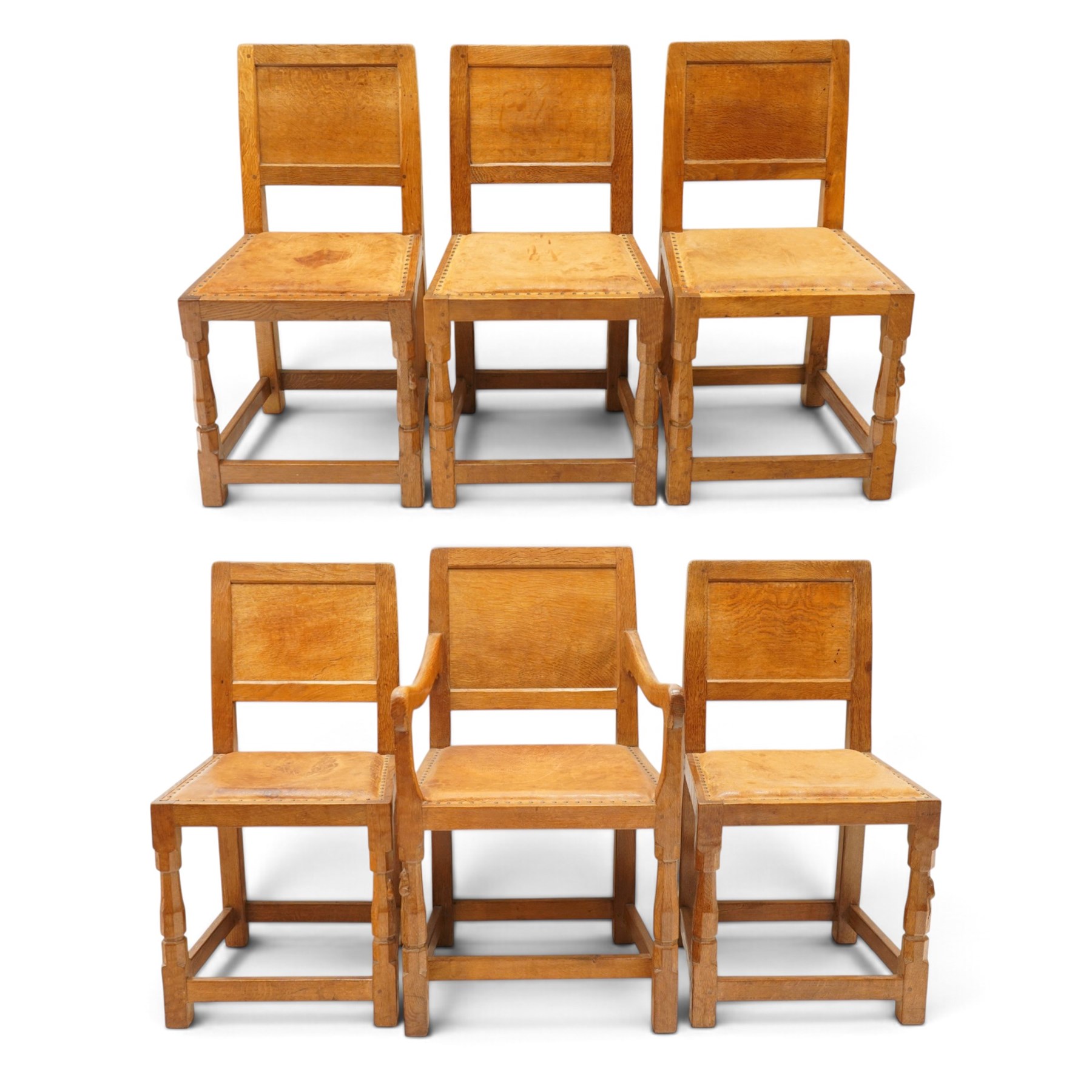 Mouseman - set of six (5+1) 1940s pre-war panel-back dining chairs, the raised backs with adzed panels, over seats upholstered in tan leather with studwork border, raised on octagonal turned baluster supports united by box stretcher, with carved mouse signature, by the workshop of Robert Thompson of Kilburn

Provenance: ordered directly from the Mouseman workshop in the 1940s before the outbreak of the war, the items were subsequently delivered after the end of war. 