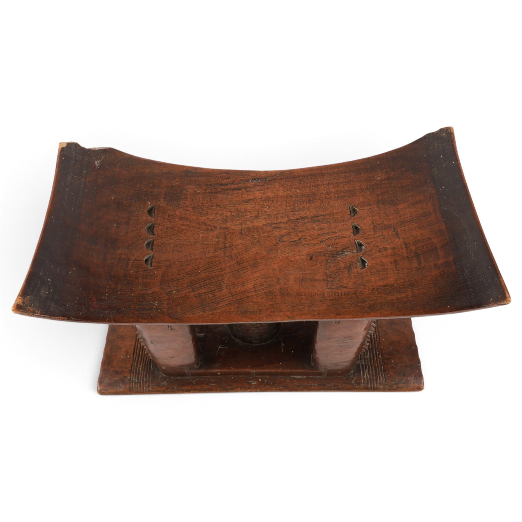 African carved hardwood headrest, having flared edges, raised on a stepped plinth base with further carved detailing, H34cm