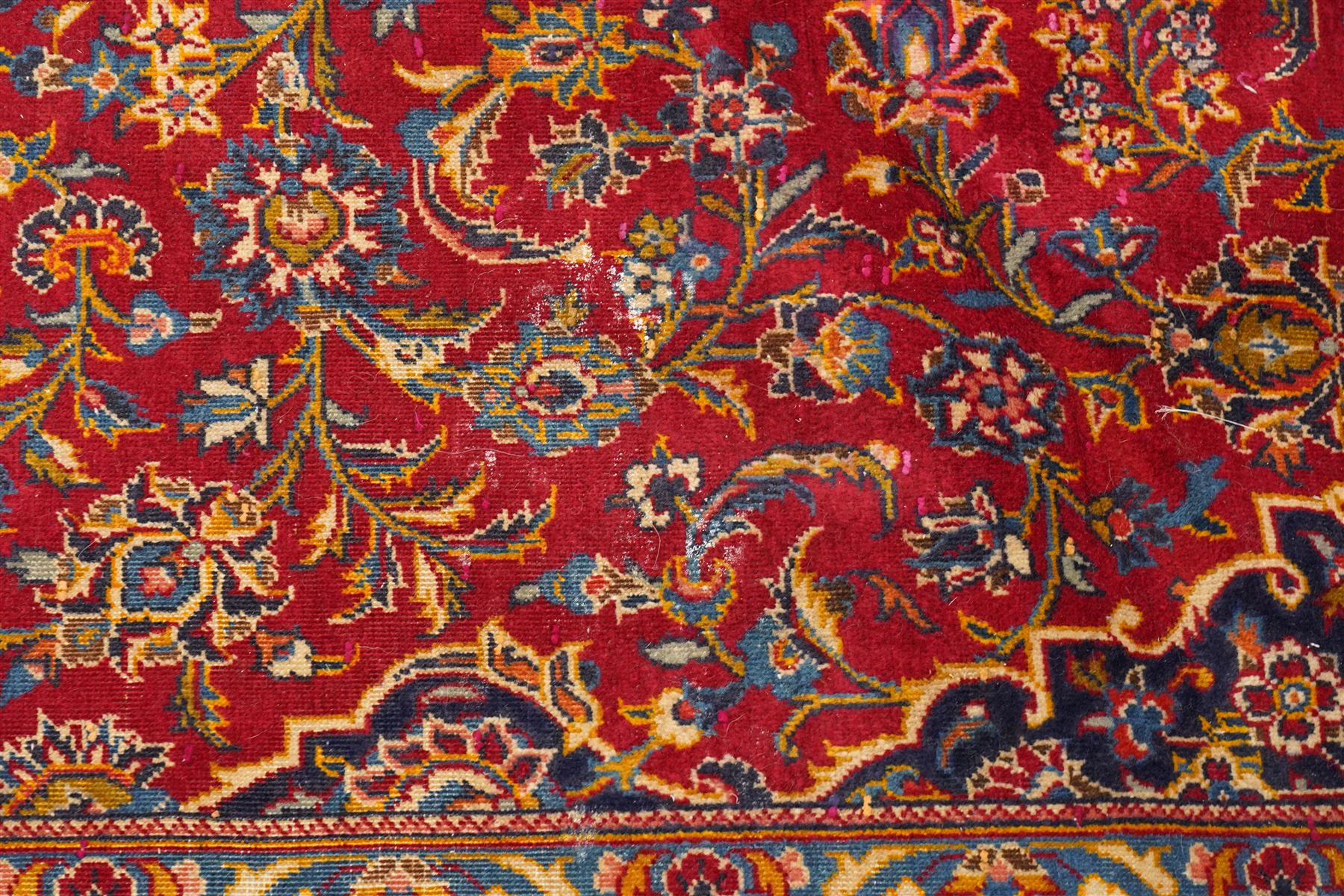 Persian Kashan hand-knotted carpet, madder red ground centred by shaped dark navy, ivory and pale blue floral medallion with pendants, surrounded by scrolling vines, palmettes and flowerheads, dark navy spandrels, enclosed by dark navy floral border with multiple floral guard stripes