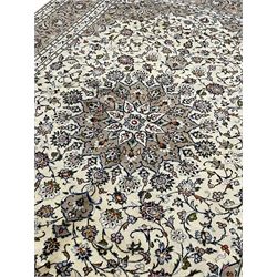 Persian Kashan ivory ground rug, central pointed rosette medallion surrounded by scrolling branches and stylised flower heads, the border with scrolling pattern decorated with palmettes, within guard stripes