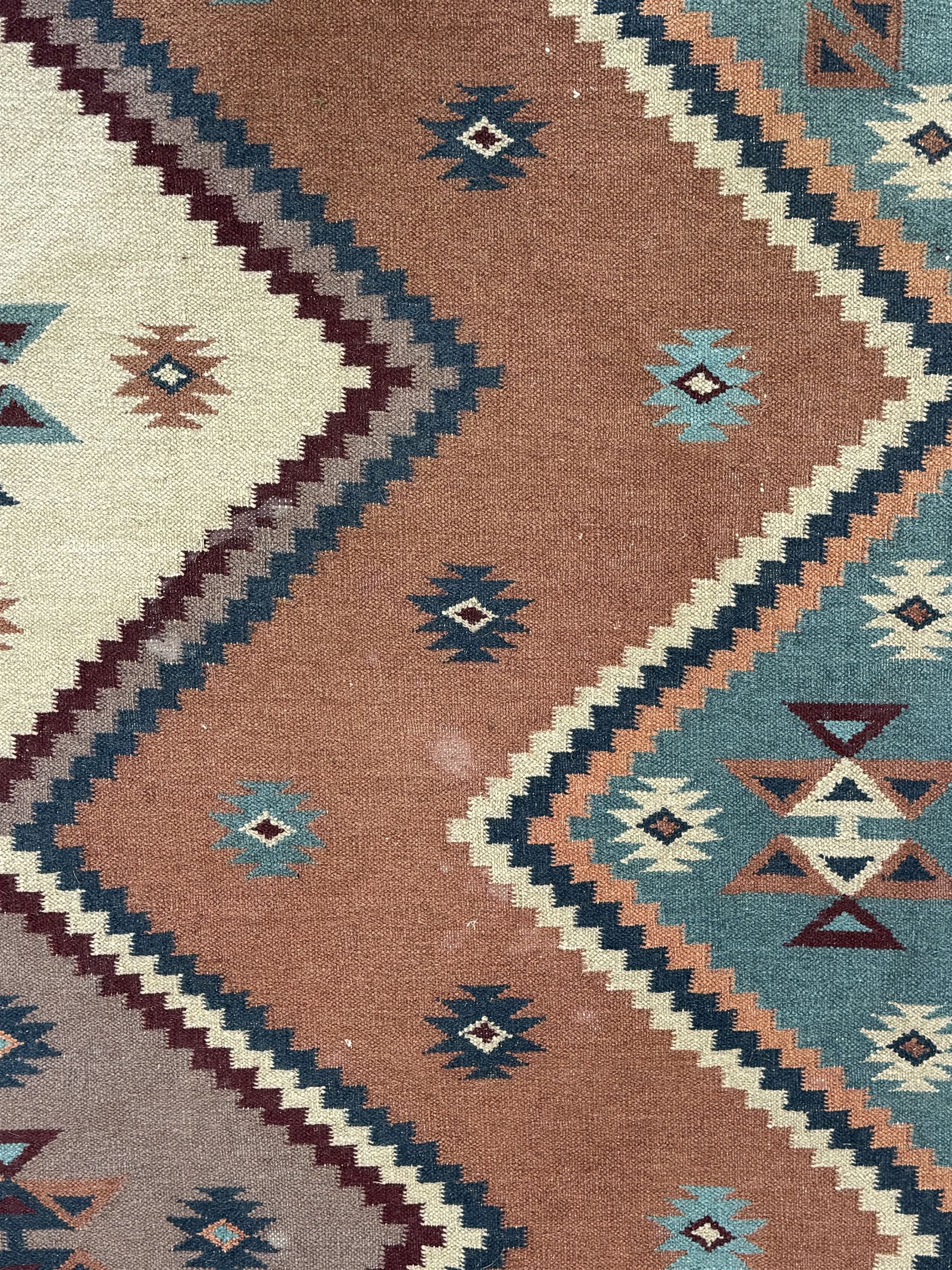 Flatweave rug, terracotta ground with multicoloured geometric diamond motifs, framed by a teal and burgundy border, finished with fringed edges