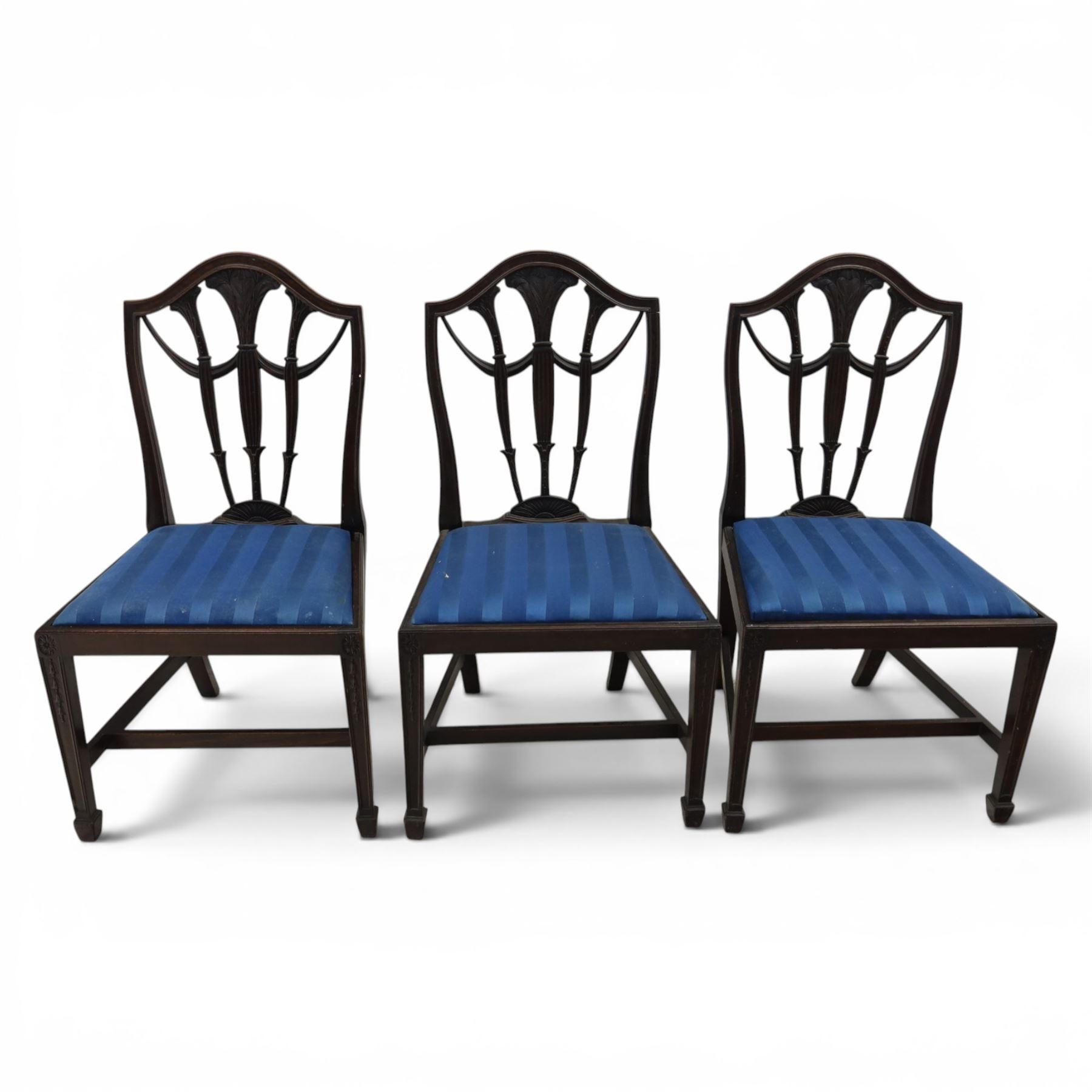 Set of eight George III style mahogany dining chairs, comprising two carvers and six singles, each with shaped top rail above pierced splay carved with feathers, with drop in stuffover seats upholstered in blue striped fabric, raised upon square tapering legs joined by stretchers, together with a mahogany twin pedestal dining table, the oval top with central leaf raised upon turned columns and splayed reeded legs terminating in lion paw feet and brass castors, 