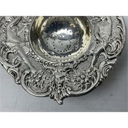 Continental white metal strainer, of shaped form embossed with classical figures, putto, musical trophies and fruiting vines, indistinctly marked, L12.5cm