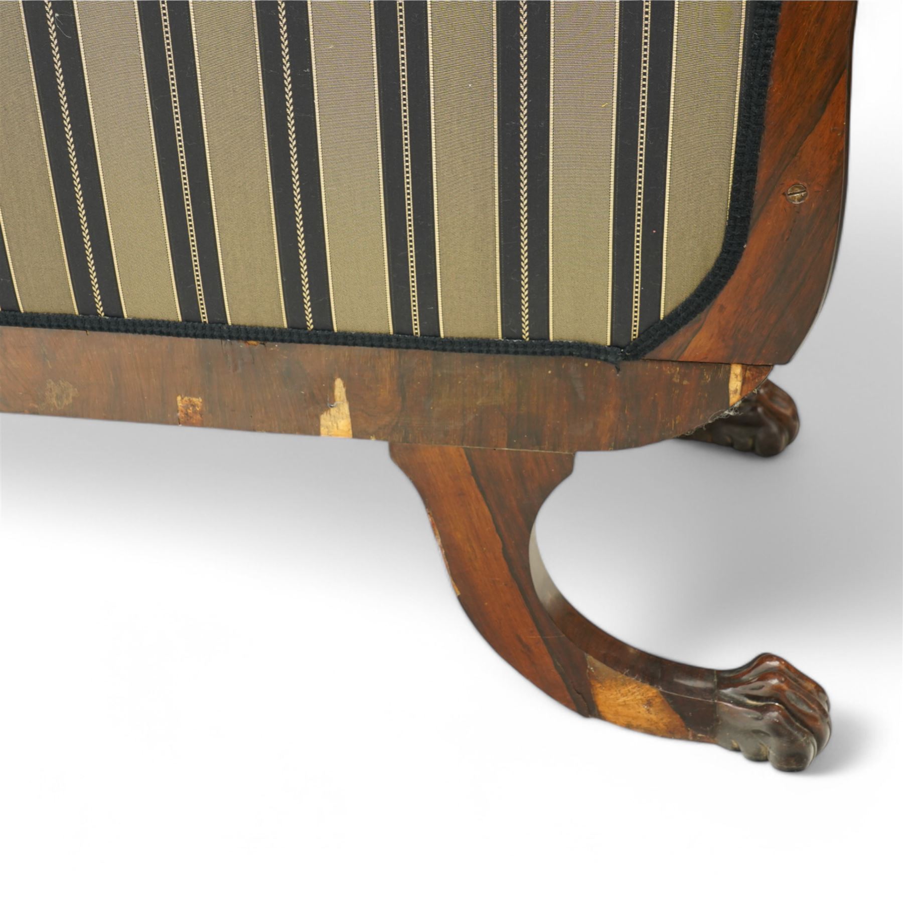 Regency brass inlaid rosewood chaise lounge or settee, shaped back over rolled head and foot, upholstered in black and gold striped fabric with rectangular squab cushion and bolster cushion, the rolled terminals carved with acanthus leaf roundels, lower rectangular foliate carved panels, on out splayed supports with paw carved feet 