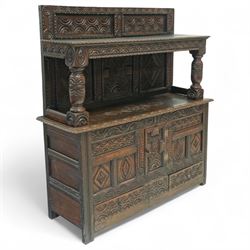 An early 20th-century Jacobean revival style carved oak Court Cupboard, tier-form of 17th-century design, rectangular form with carved back with geometric motifs and arches, projecting top section over twin baluster columns connecting the lower tier above a carved panelled front and panelled cupboard door with profusely carved lozenges and lunettes, above two base drawers, raised on block feet 