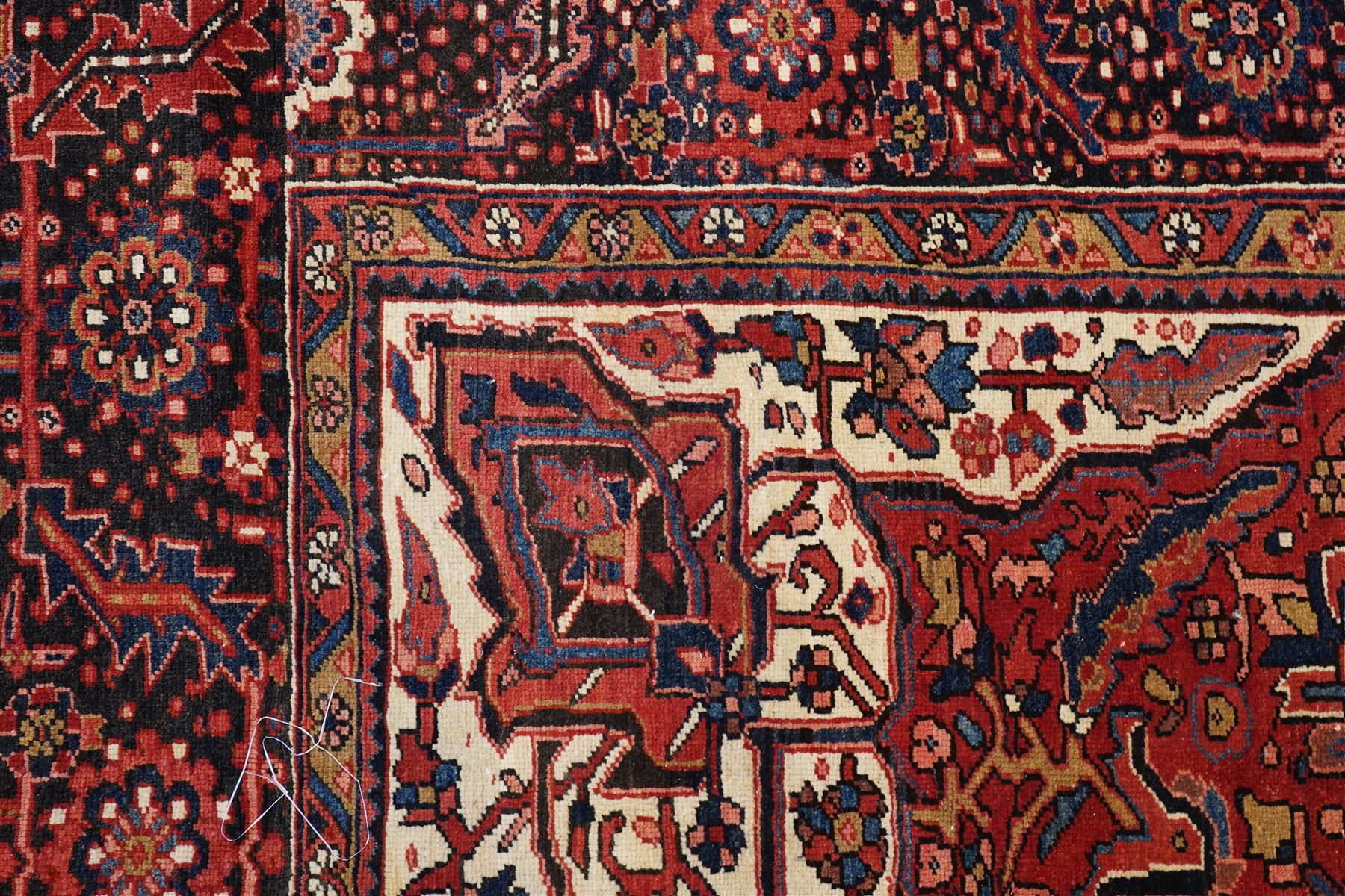 North West Persian Heriz/Ahar hand-knotted carpet, brick red field with a central bold stepped star medallion with pendants, surrounded by angular floral and geometric motifs, ivory spandrels, enclosed by a dark indigo border of stylized rosettes and vine motifs with multiple guard stripes, cotton fringe ends 